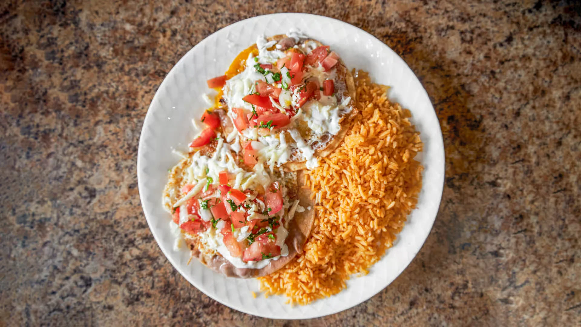 A traditional plate of Huevos Rancheros at El Ranchito Poblano, featuring fried eggs over tortillas topped with salsa and cheese, with a side of Mexican rice.