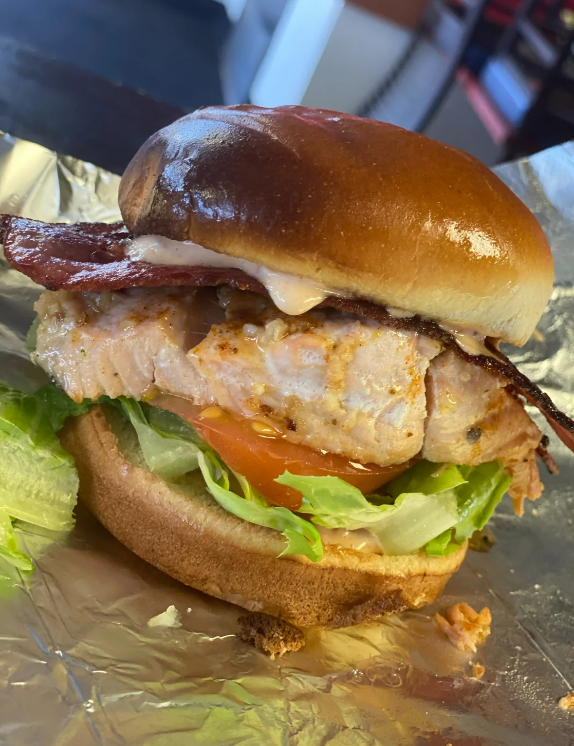 A salmon burger topped with bacon, lettuce, and tomato, served on a toasted bun.