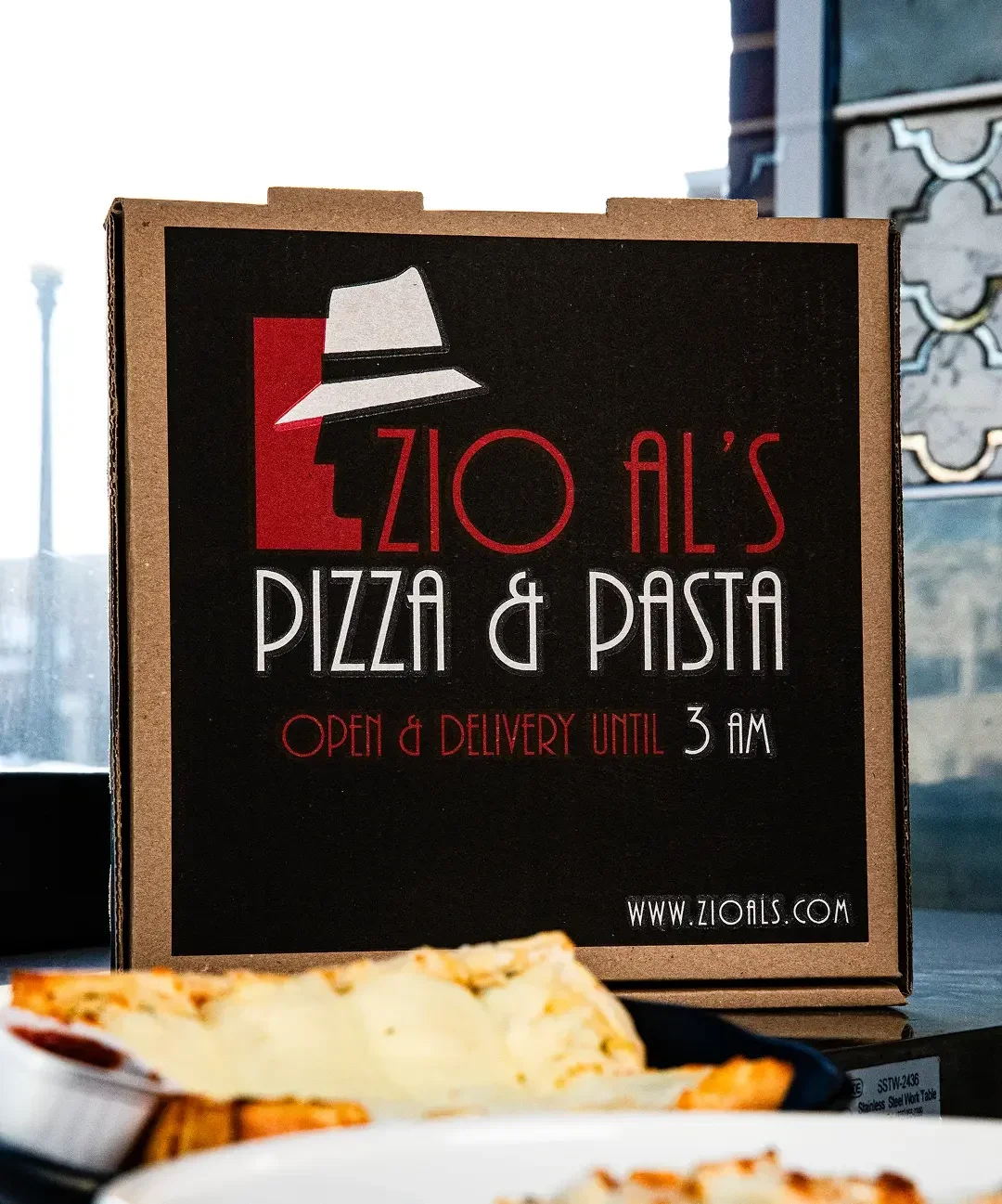 Zio Al's Pizza & Pasta delivery box with food items on a table.