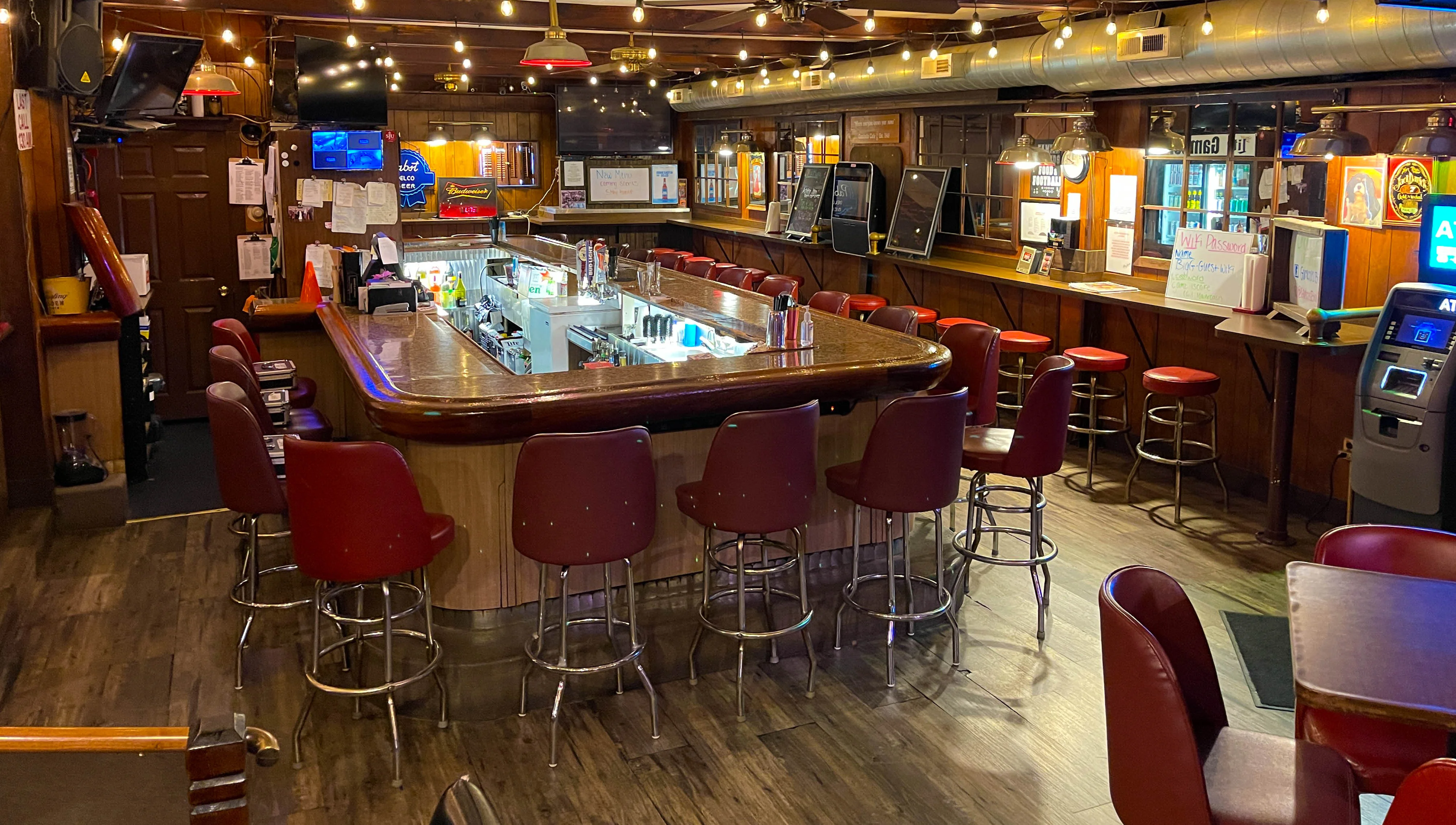 A spacious bar showcasing a polished counter, red seating, and various bottles behind the bar. The warm lighting creates a welcoming atmosphere.