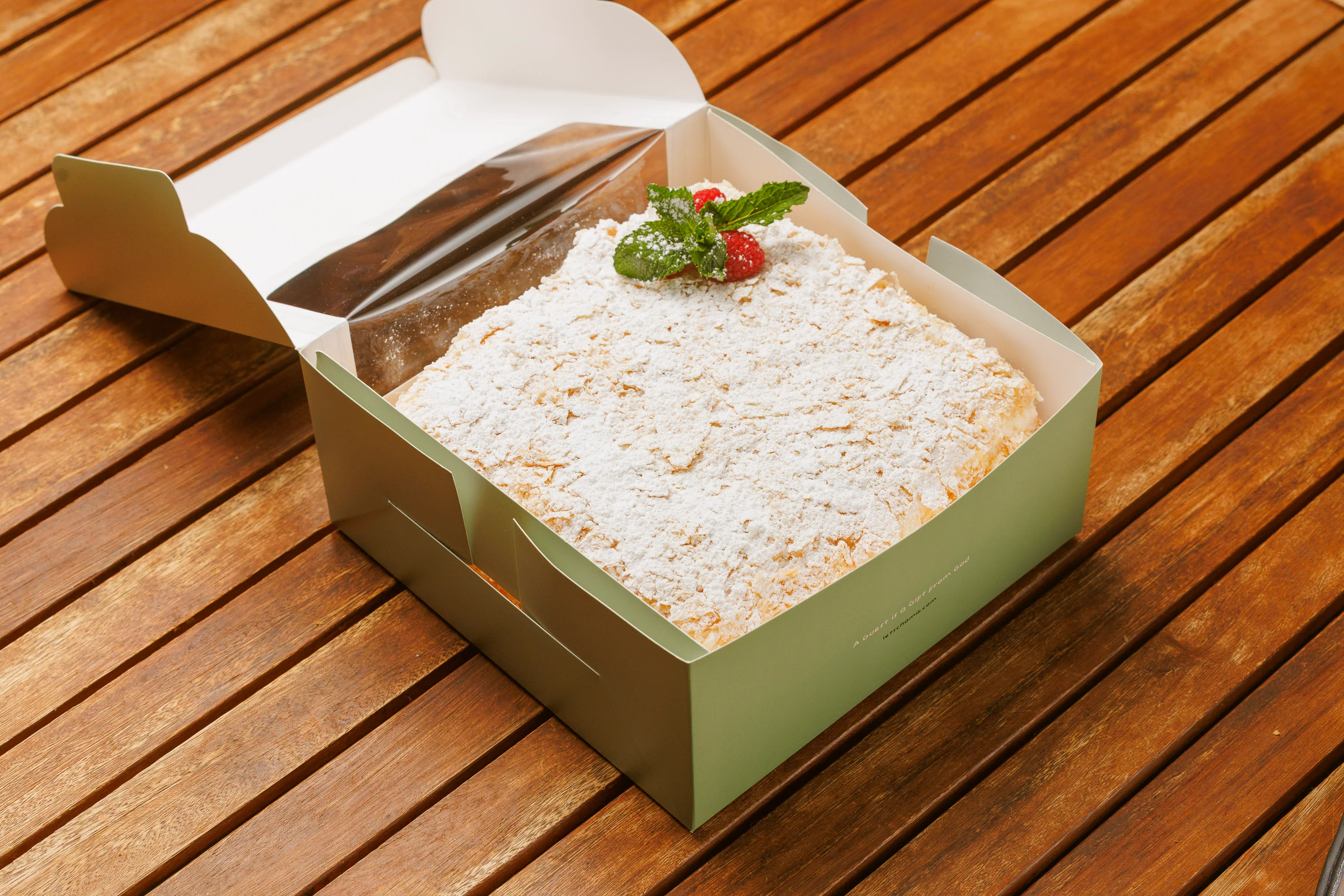 Powdered sugar Napoleon pastry with mint and raspberry in a bakery box