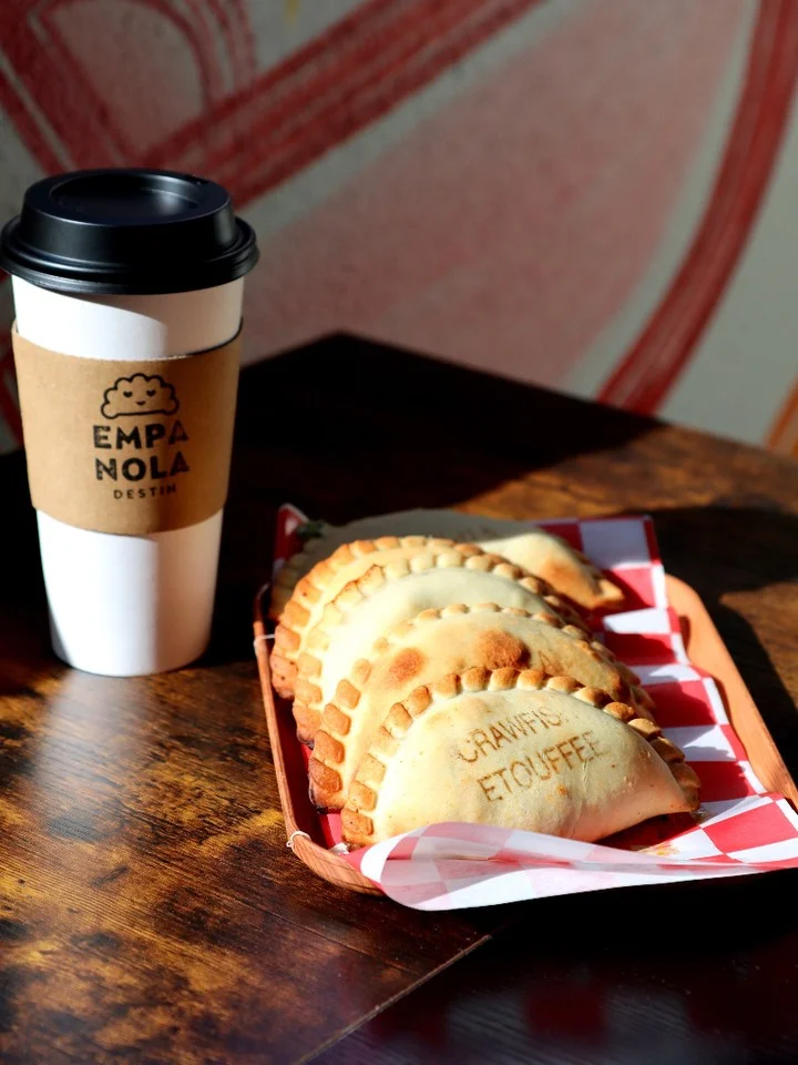 A coffee cup next to a tray of empanadas with a checkered paper lining, displaying a variety of flavors.