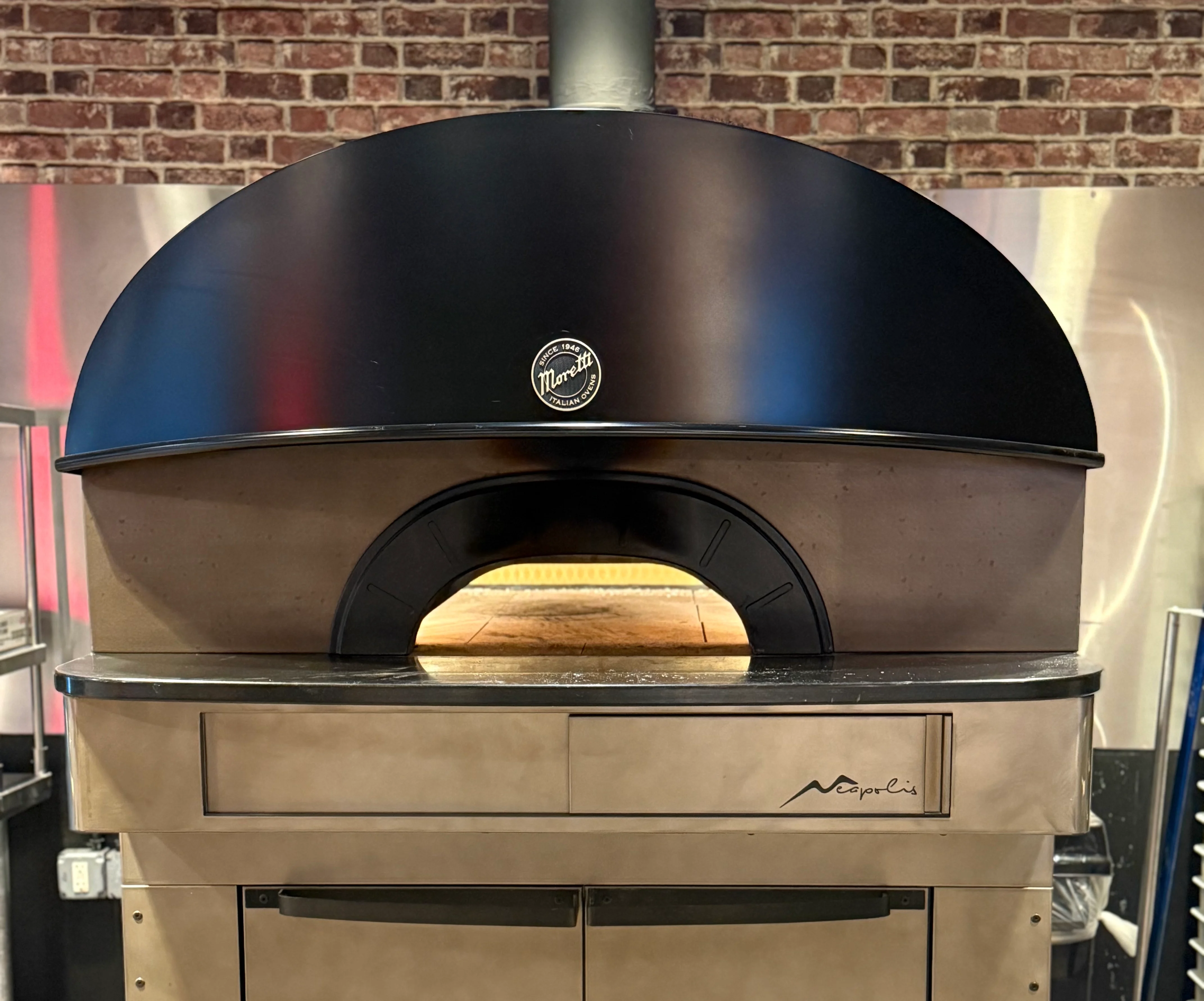 Wood-fired pizza oven with black dome and brick backdrop