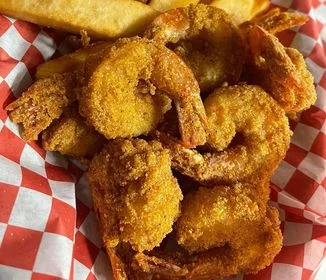 A serving of golden fried shrimp placed on a red and white checkered paper alongside crispy French fries.