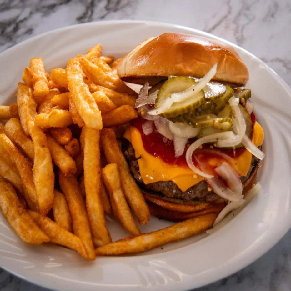 A classic hamburger with melted cheese, pickles, onions, and ketchup, accompanied by a side of crispy French fries.