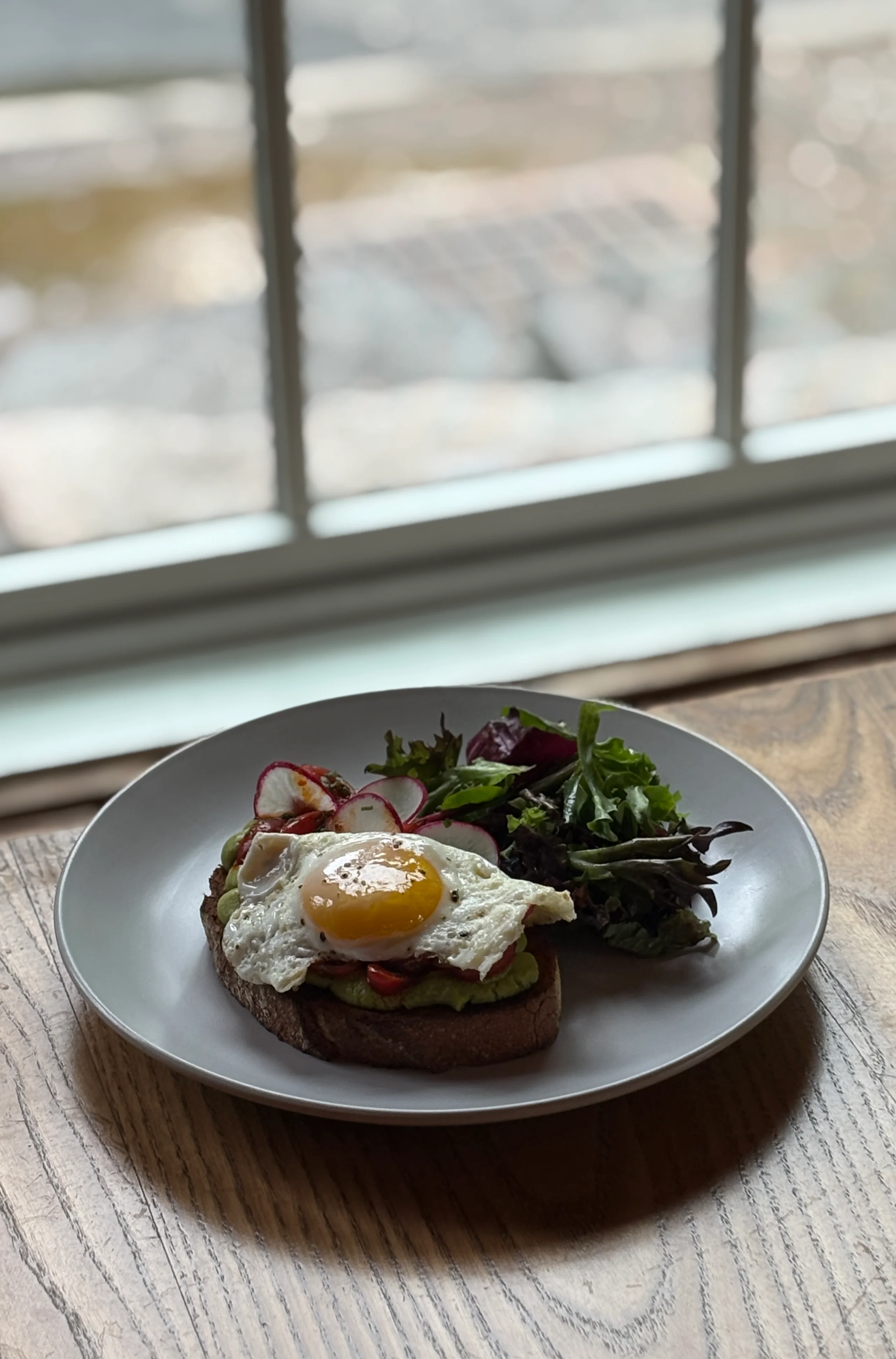 Avocado toast topped with a fried egg, served with mixed greens salad