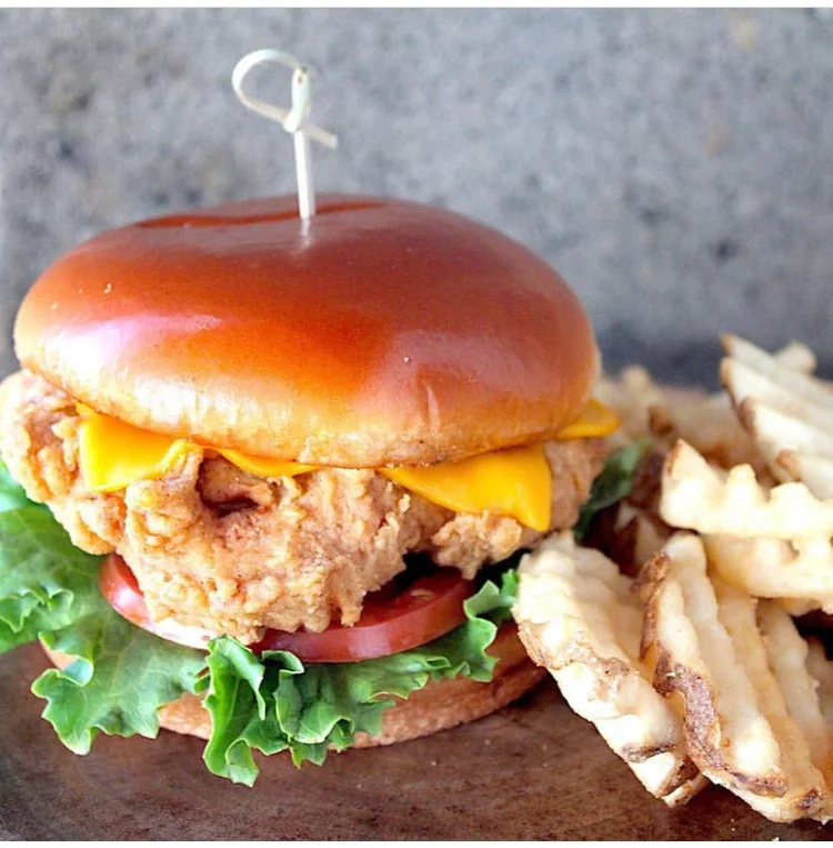 Delicious chicken sandwich with toppings on a wooden table