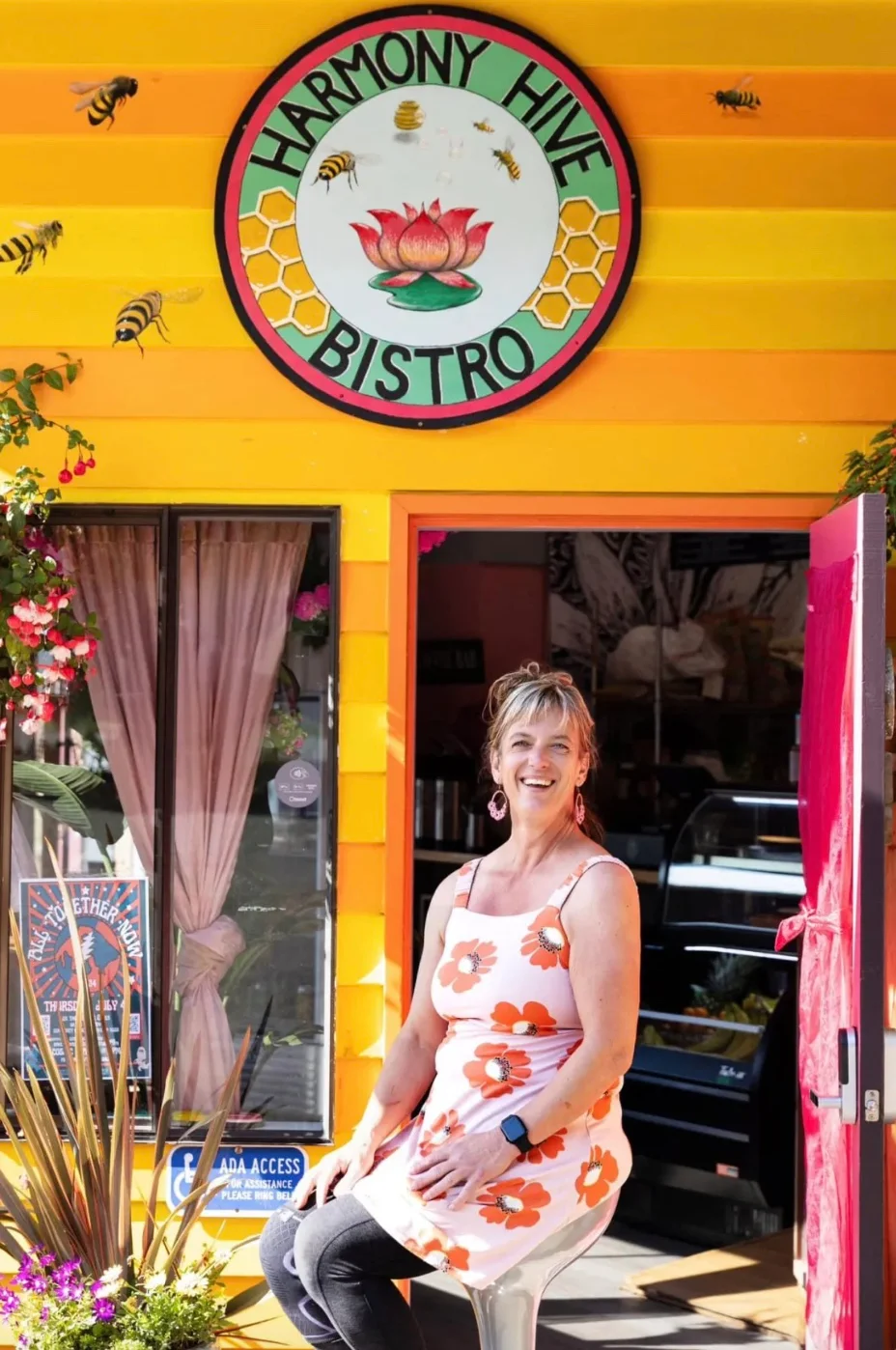 Owner of Harmony Hive Bistro smiling at the colorful restaurant entrance