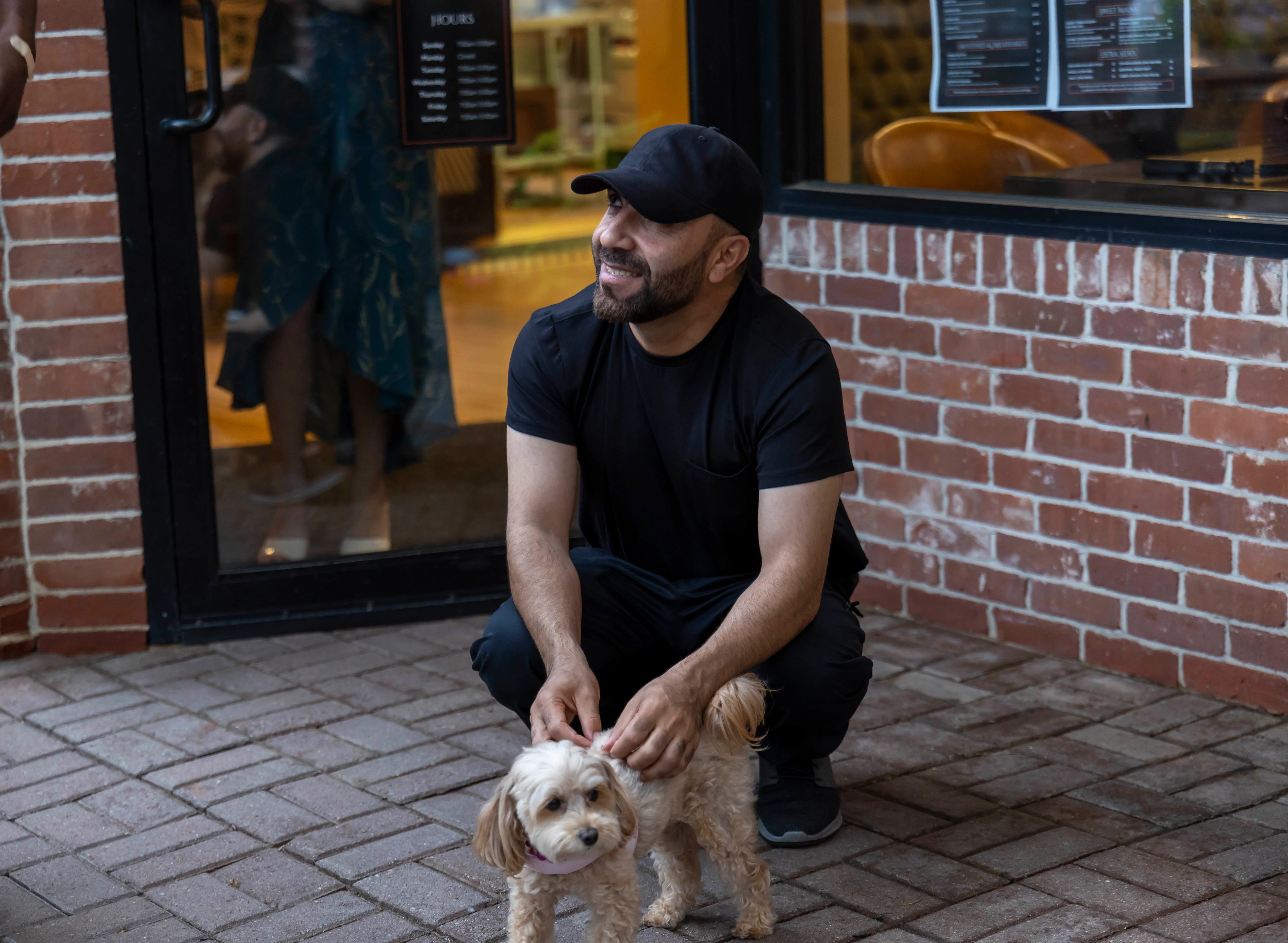 Man kneeling with a small dog outside a restaurant entrance