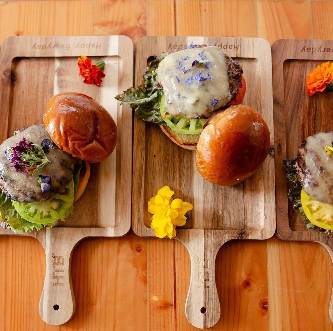 Gourmet cheeseburgers with edible flowers on wooden platters