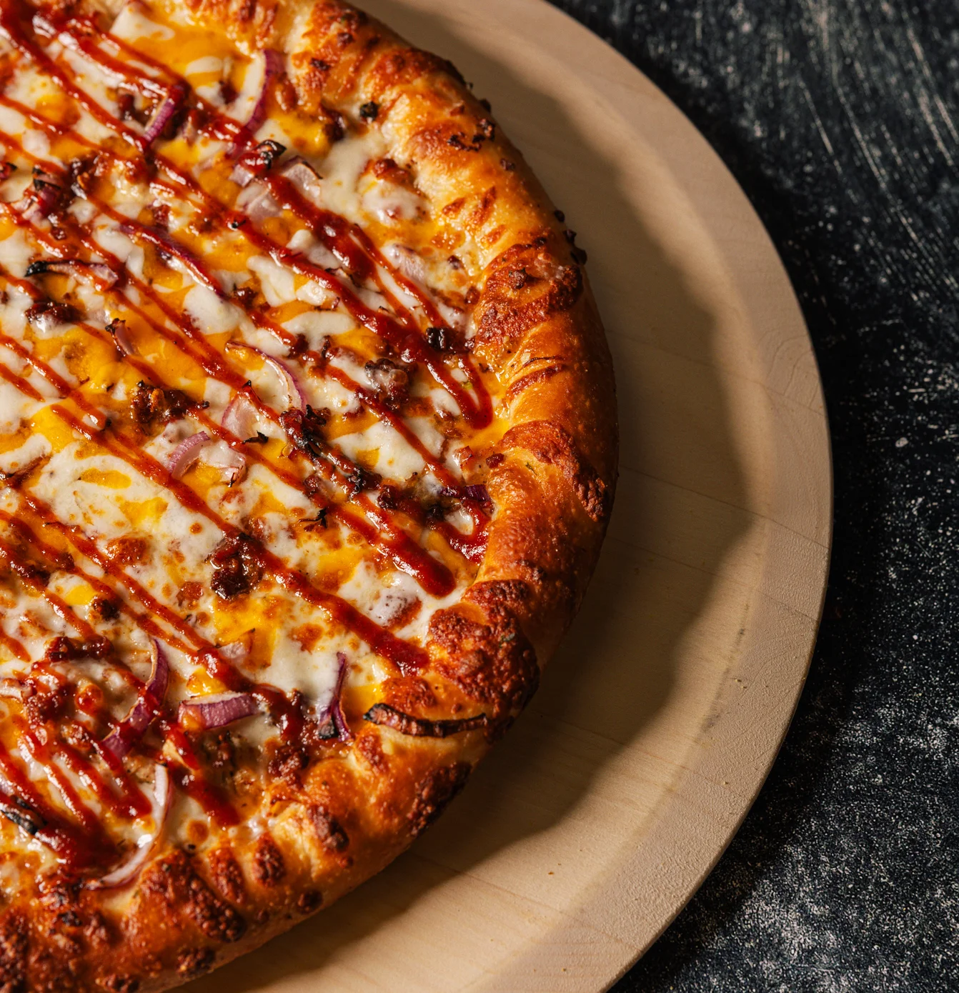 BBQ chicken pizza with drizzled sauce on a wooden serving board