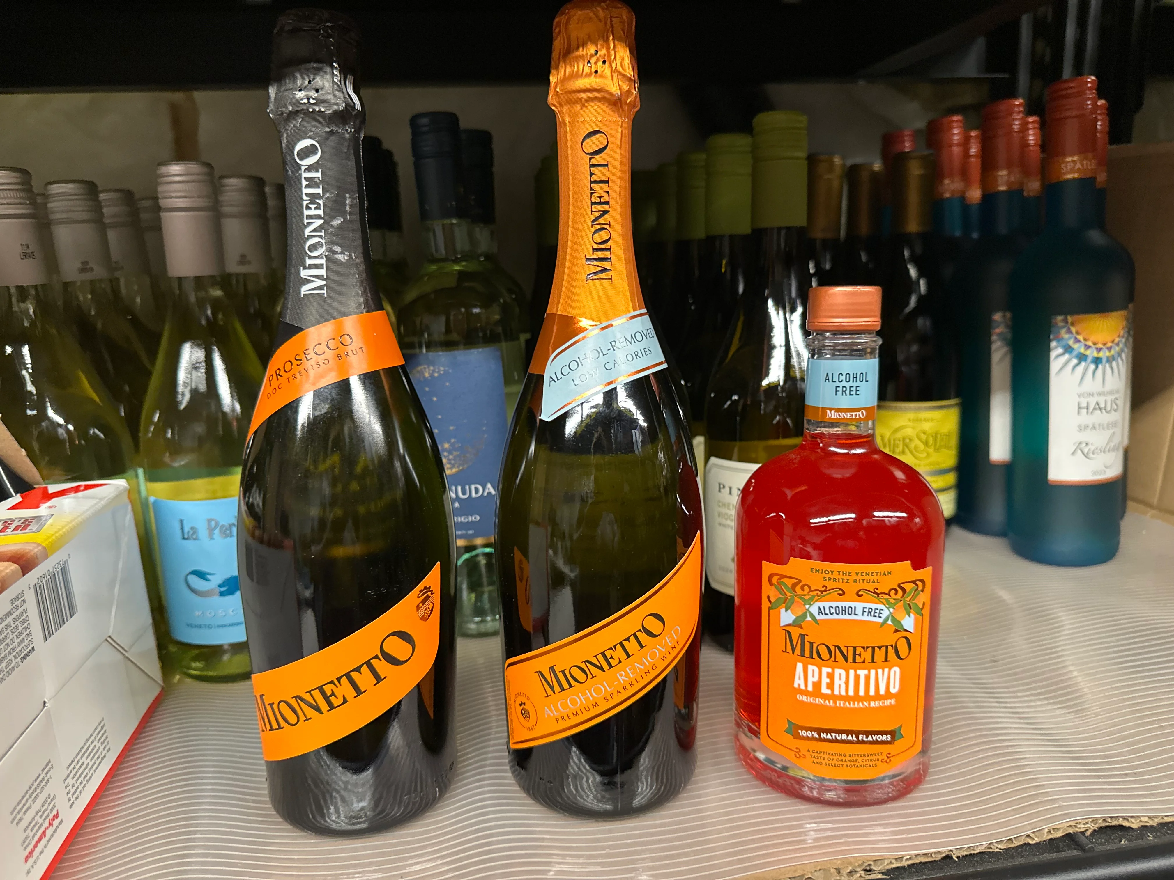 A selection of wine bottles, including sparkling wine and an alcohol-free aperitif, displayed on a shelf.