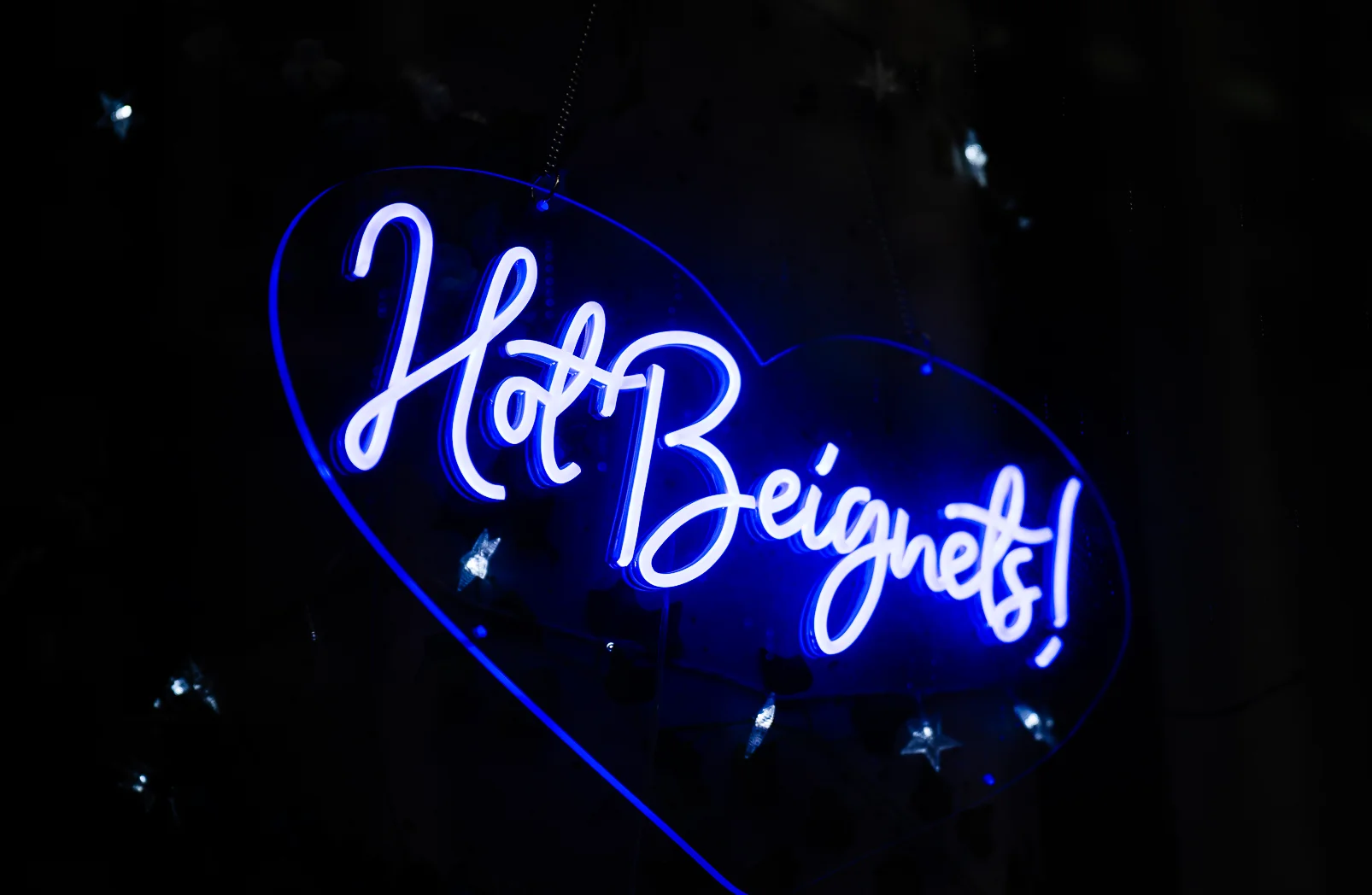Neon sign reading 'Hot Beignets!' in vibrant blue light