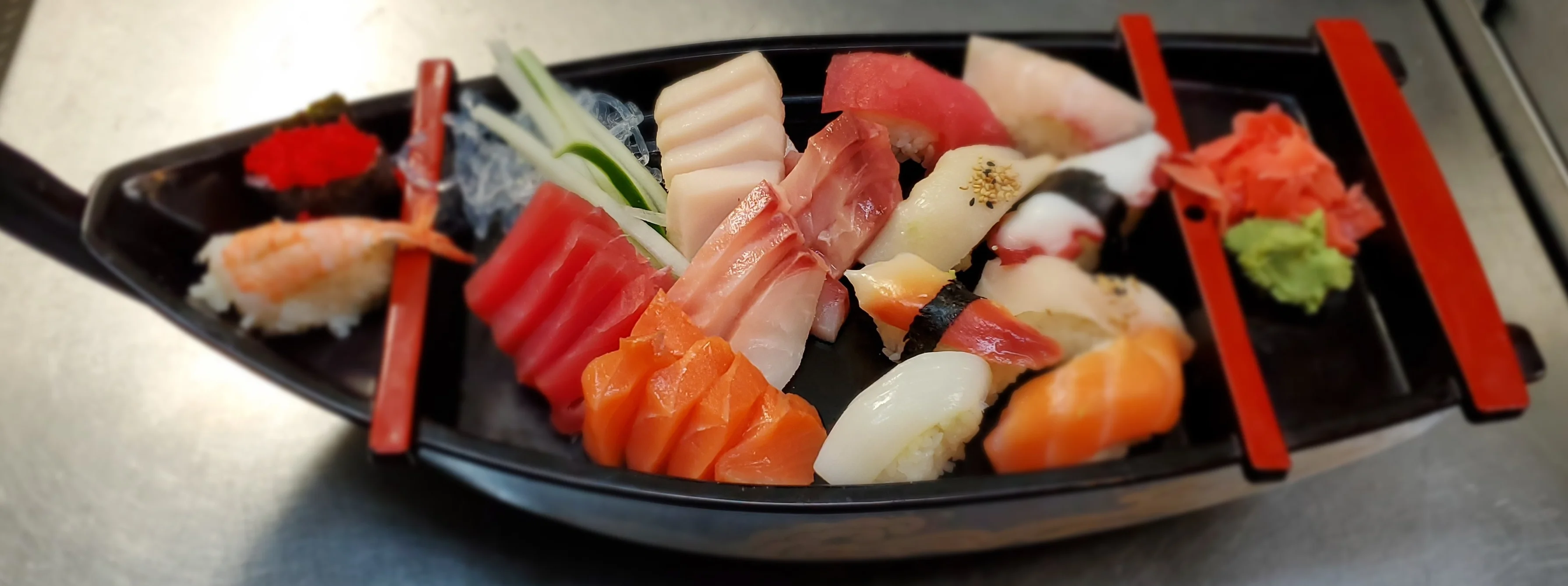 Mixed sushi and sashimi platter with fresh fish including tuna, salmon, and yellowtail on black serving plate