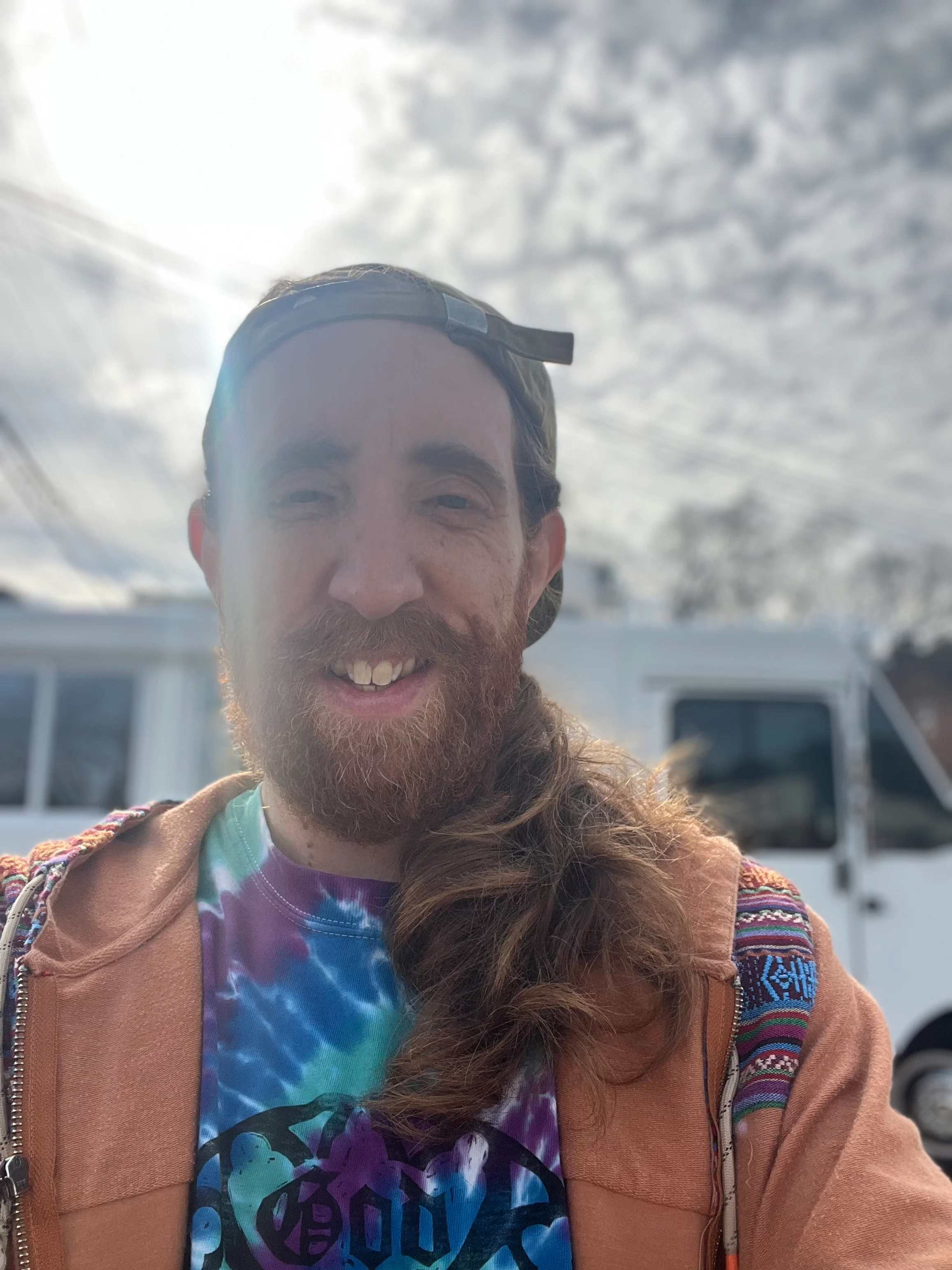 Person smiling outdoors with a colorful tie-dye shirt