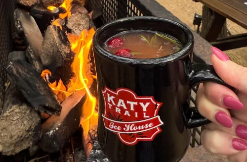 Kahlúa and tequila bottles with cocktail mug beside a glowing restaurant fireplace