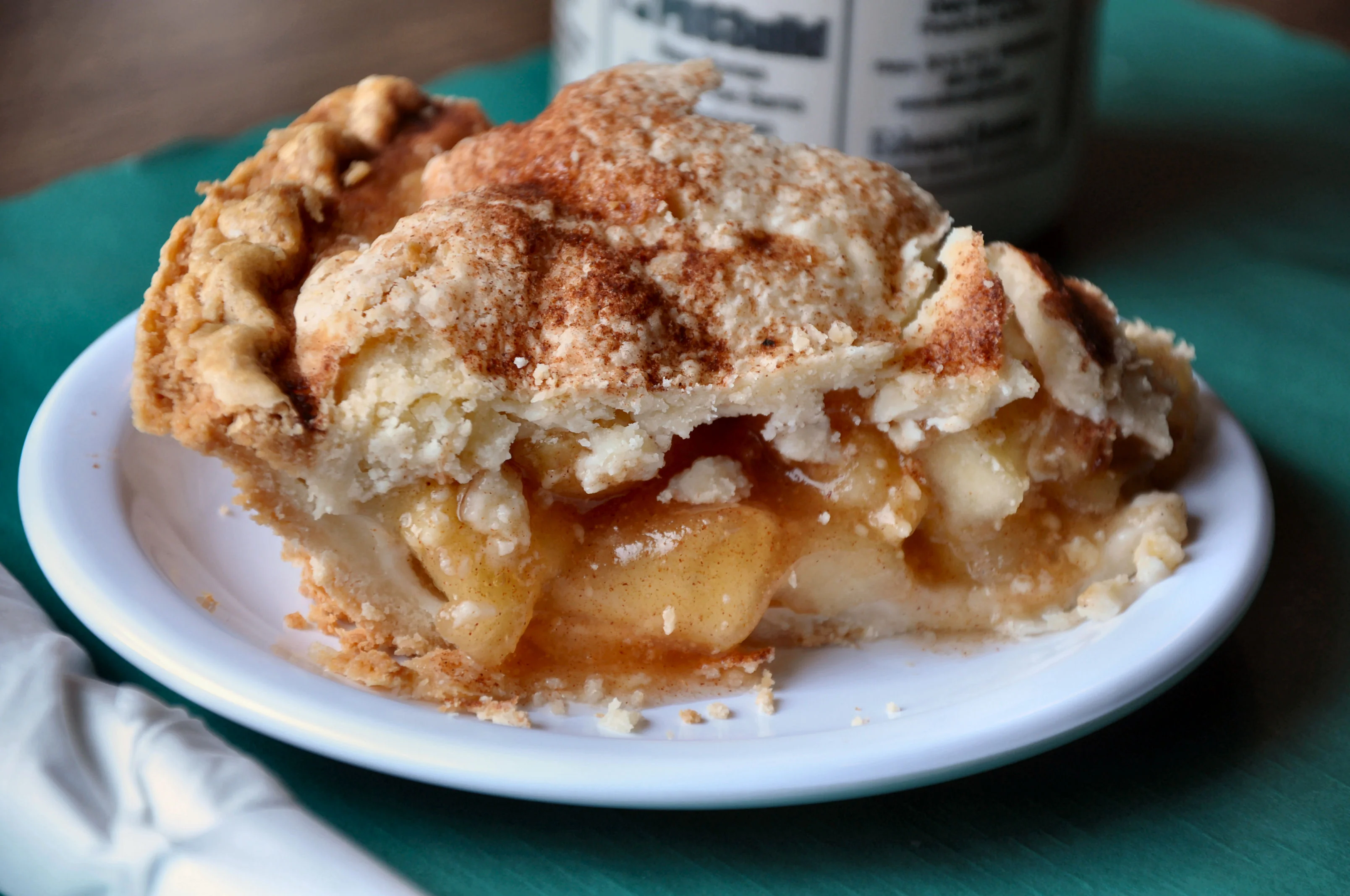A slice of apple pie displaying a flaky crust and a rich filling of cooked apples, topped with a sprinkle of cinnamon.