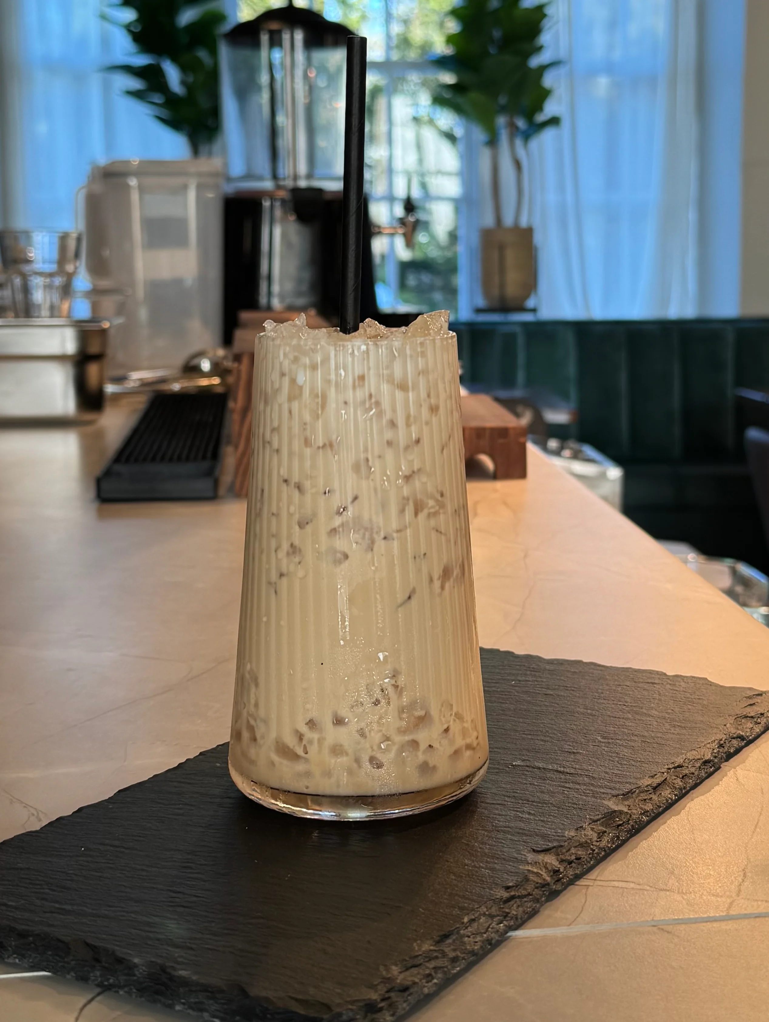 Iced beverage in a tall glass on a slate coaster at a cafe.
