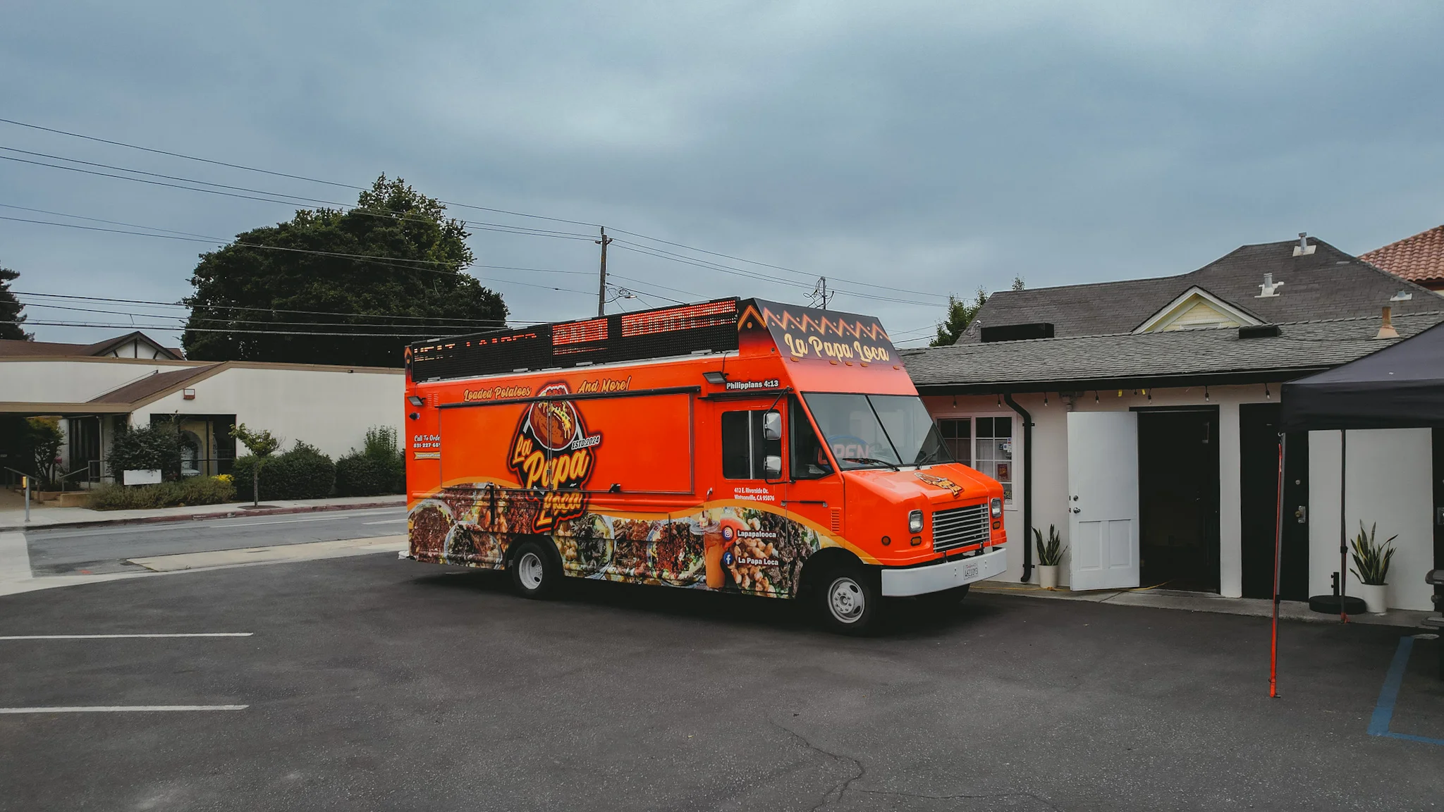 A vibrant food truck with colorful graphics, parked in an urban area near other buildings.