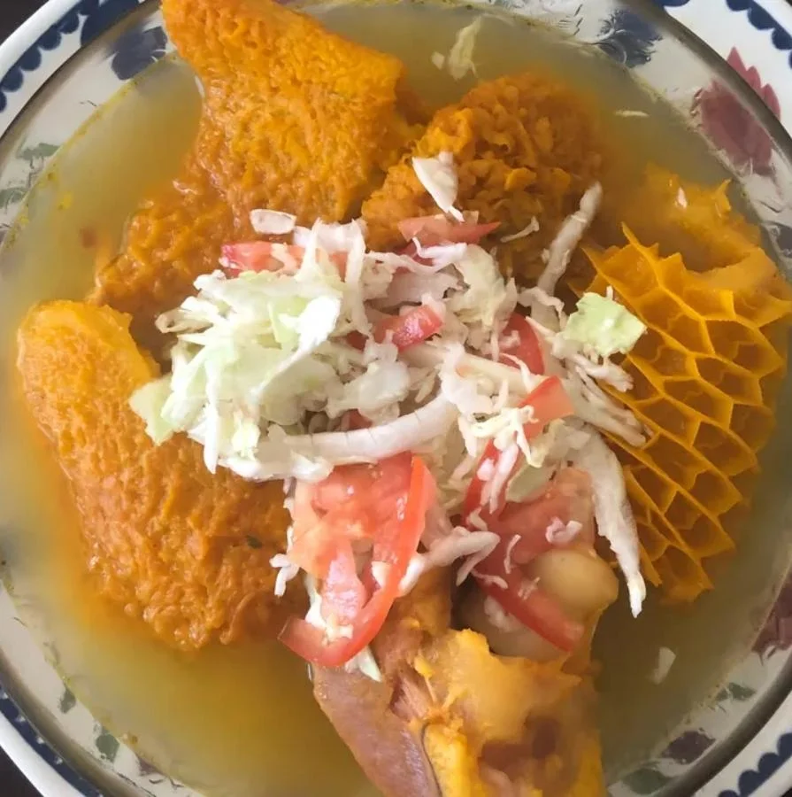 A hearty bowl of soup featuring pieces of meat, garnished with shredded cabbage and tomatoes, served in a broth.