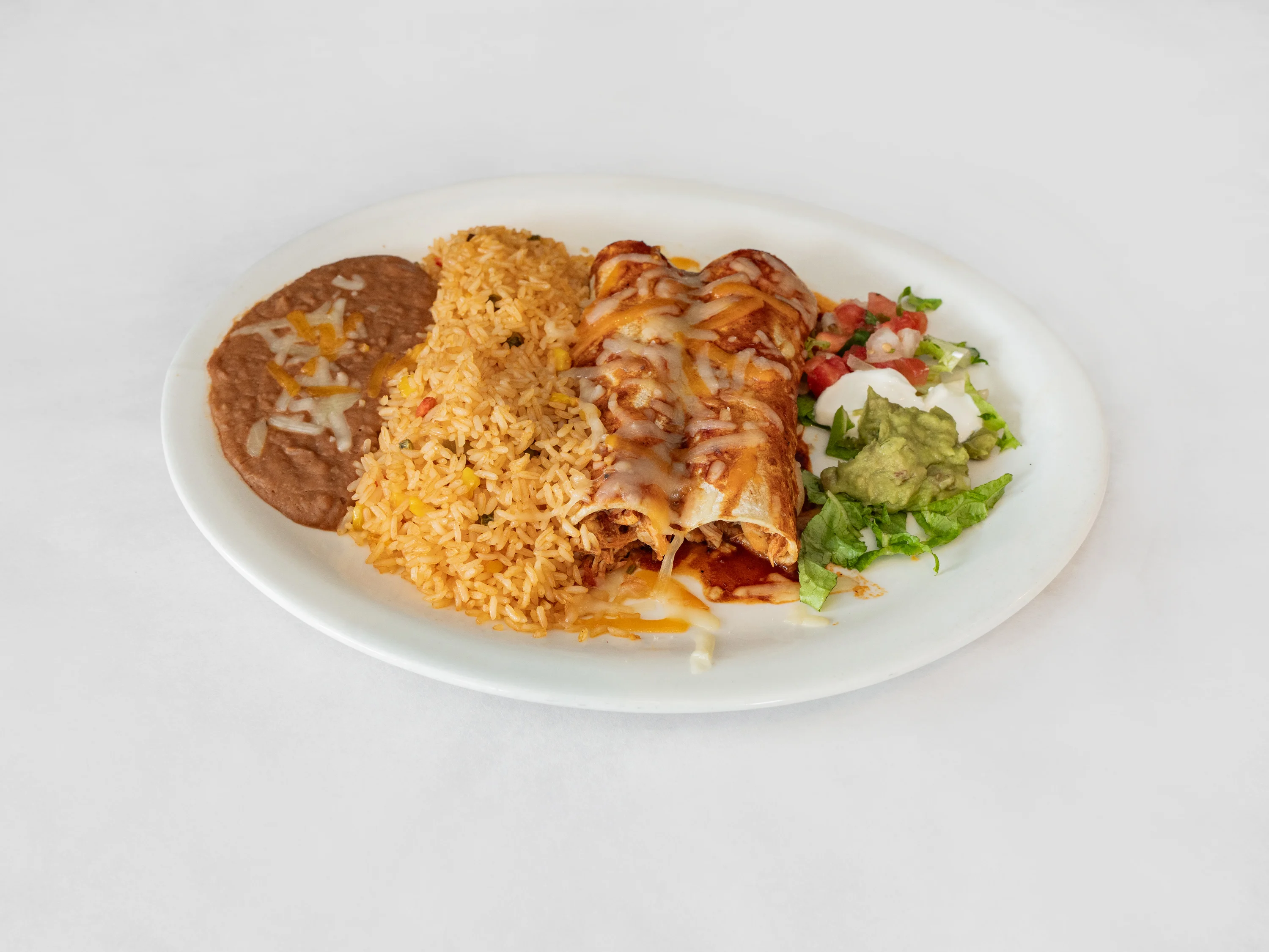 A plate featuring enchiladas topped with melted cheese, paired with Spanish rice, refried beans, and fresh toppings such as guacamole, pico de gallo, and lettuce.