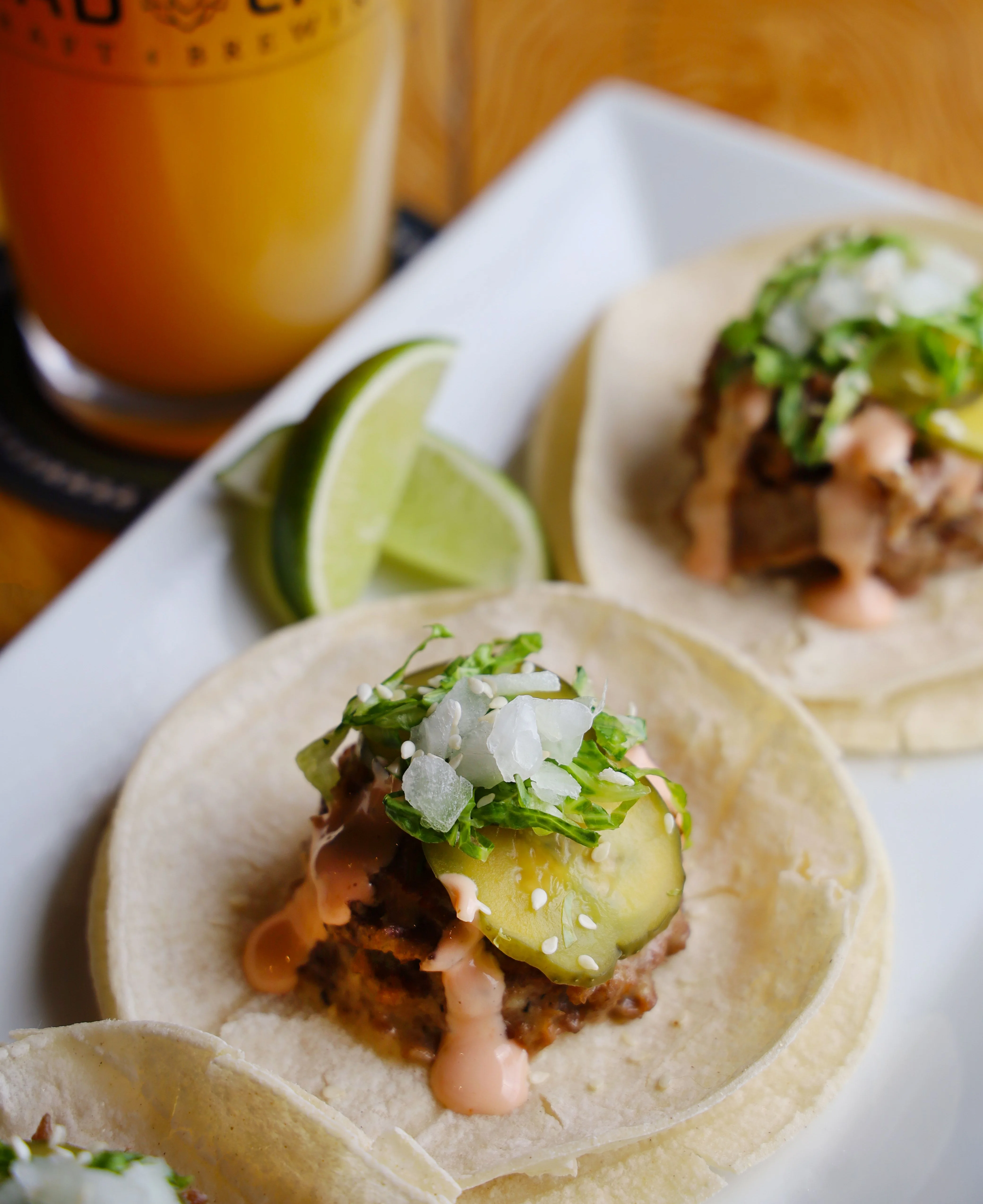 Three tacos with pulled meat, pineapple, and lime on a plate.