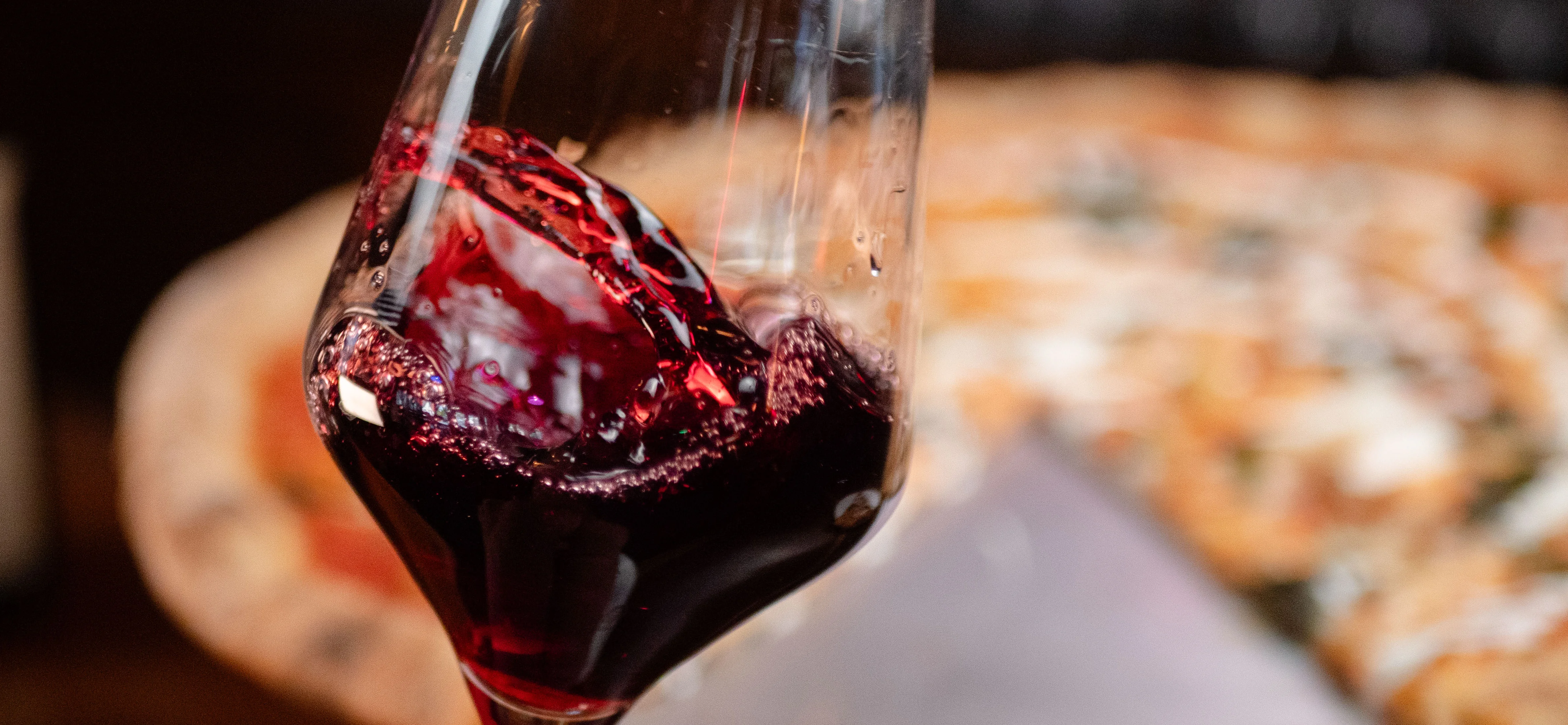a glass of wine swirls in the foreground of a partially eaten pizza