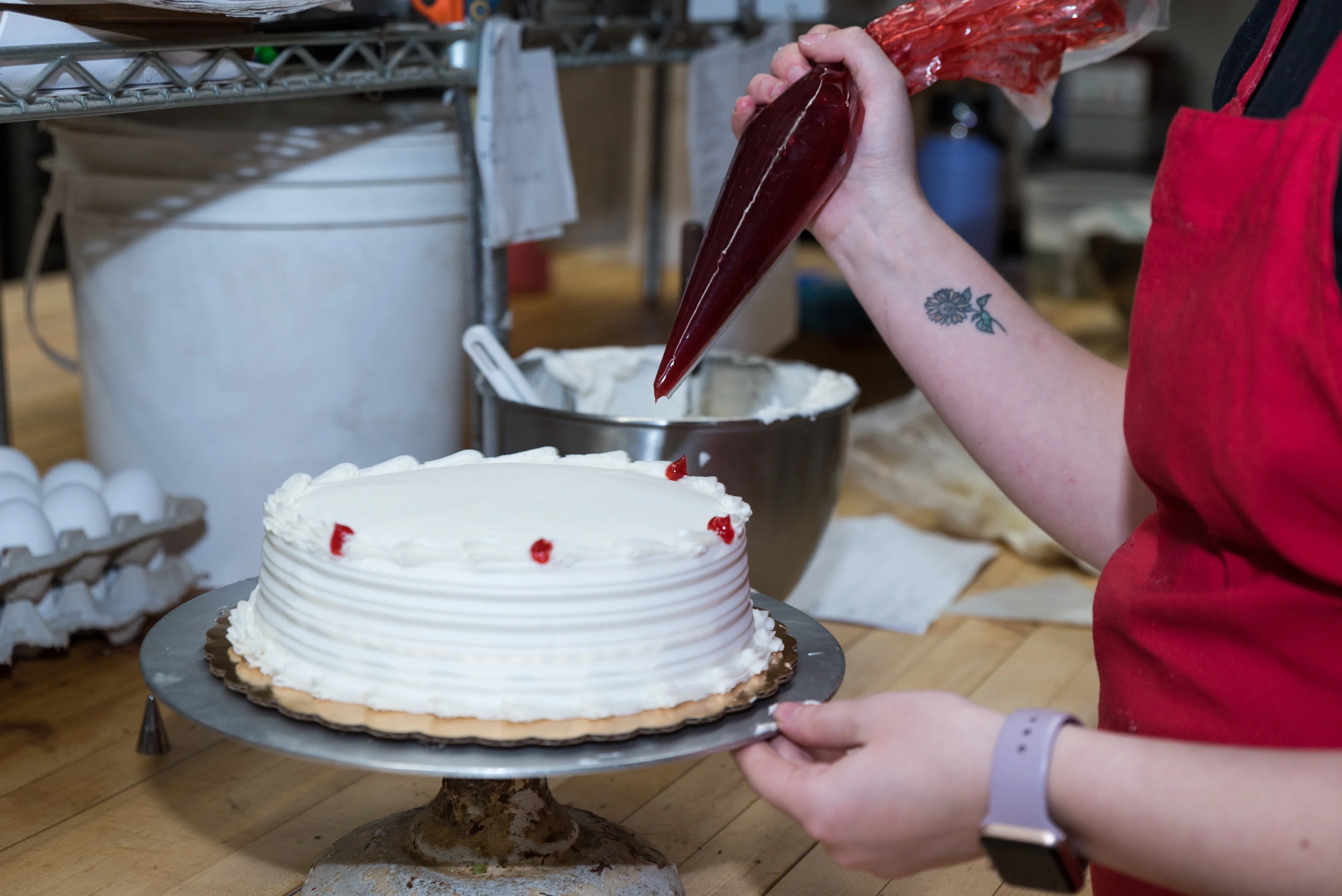 Decorating a cake with whipped cream and cherry topping in a bakery