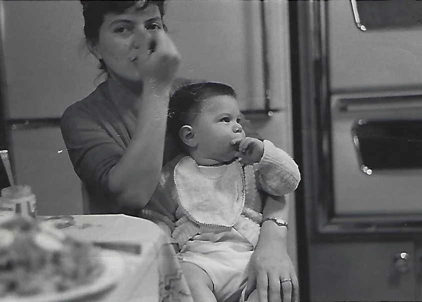 A woman holding a baby at a table with food in a cozy kitchen setting.