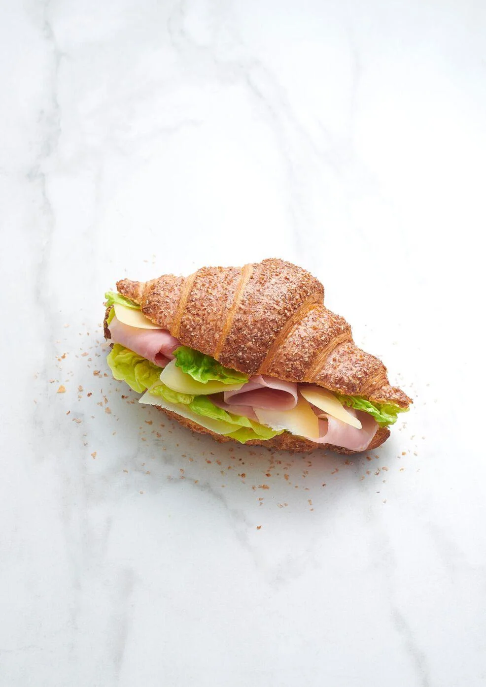 A croissant sandwich filled with ham, cheese, and lettuce, placed on a marble surface for a clean presentation.