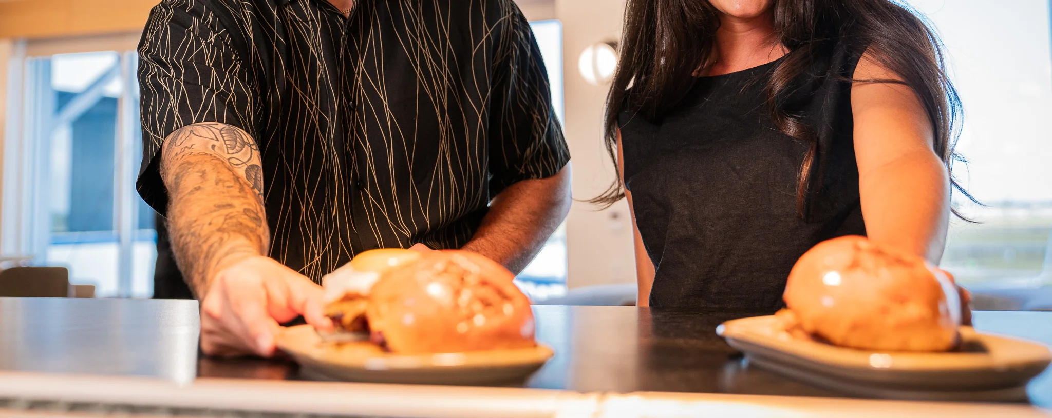 Two people serving gourmet burgers in a modern restaurant