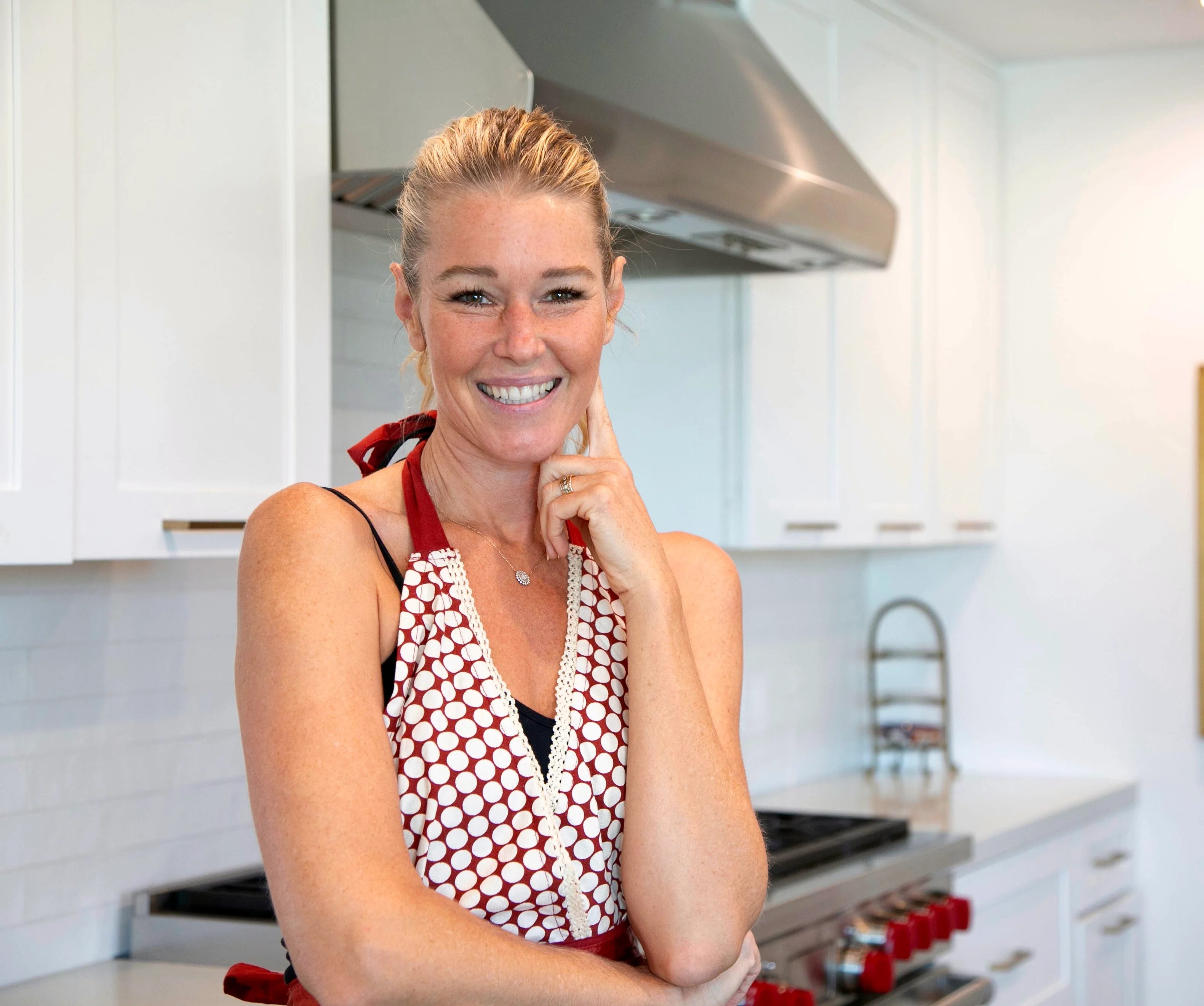 A person standing in a modern kitchen with a friendly smile, wearing a patterned apron.