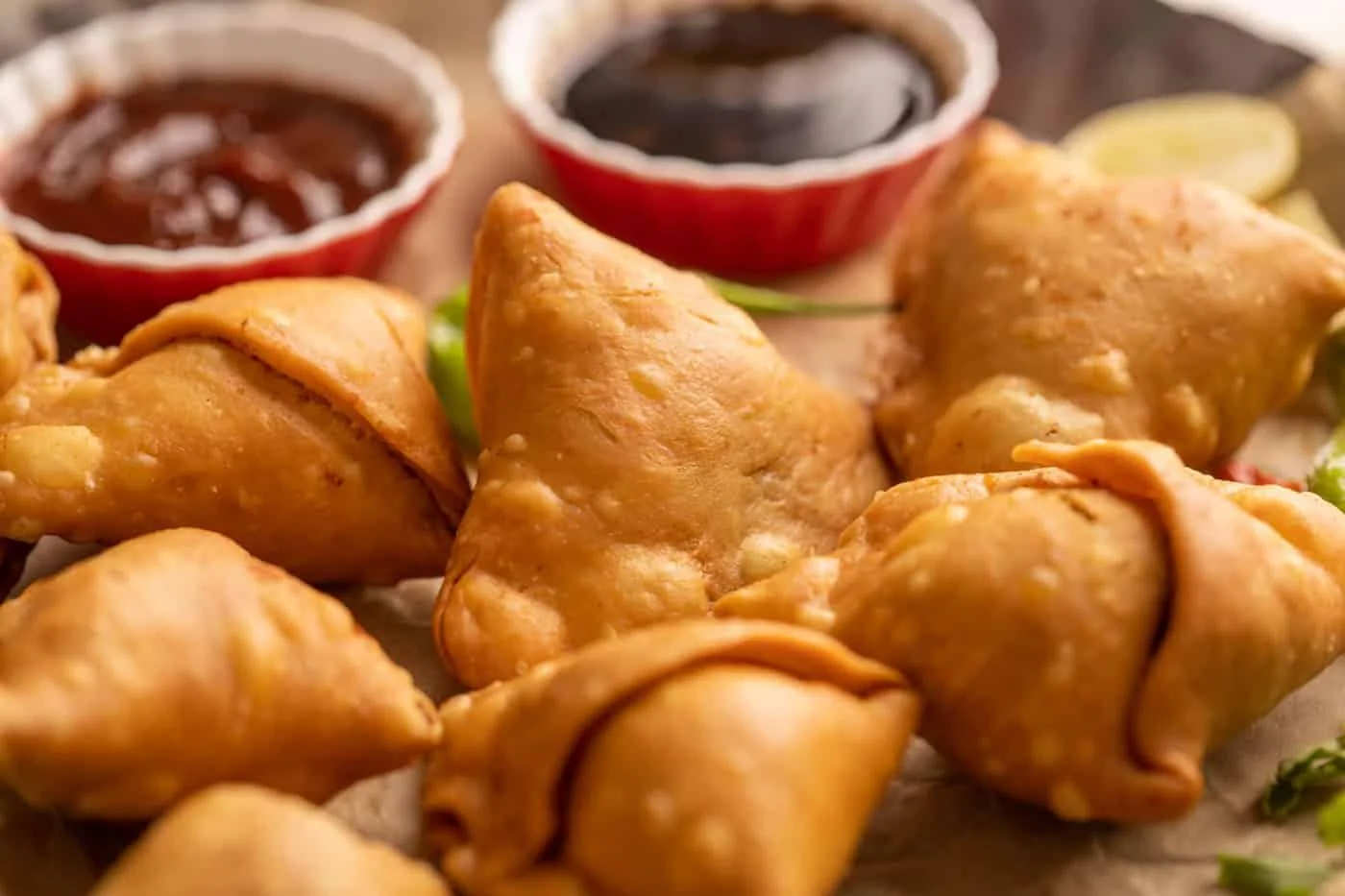 A variety of golden samosas arranged on a platter, accompanied by dipping sauces.