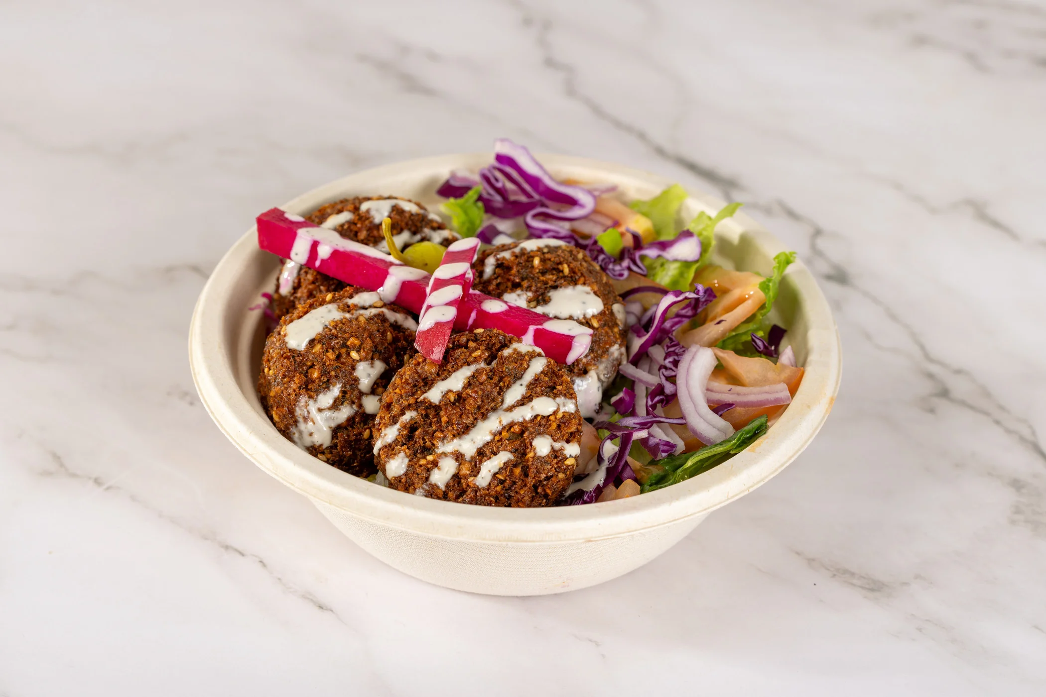 A colorful falafel bowl with fresh vegetables and sauces.