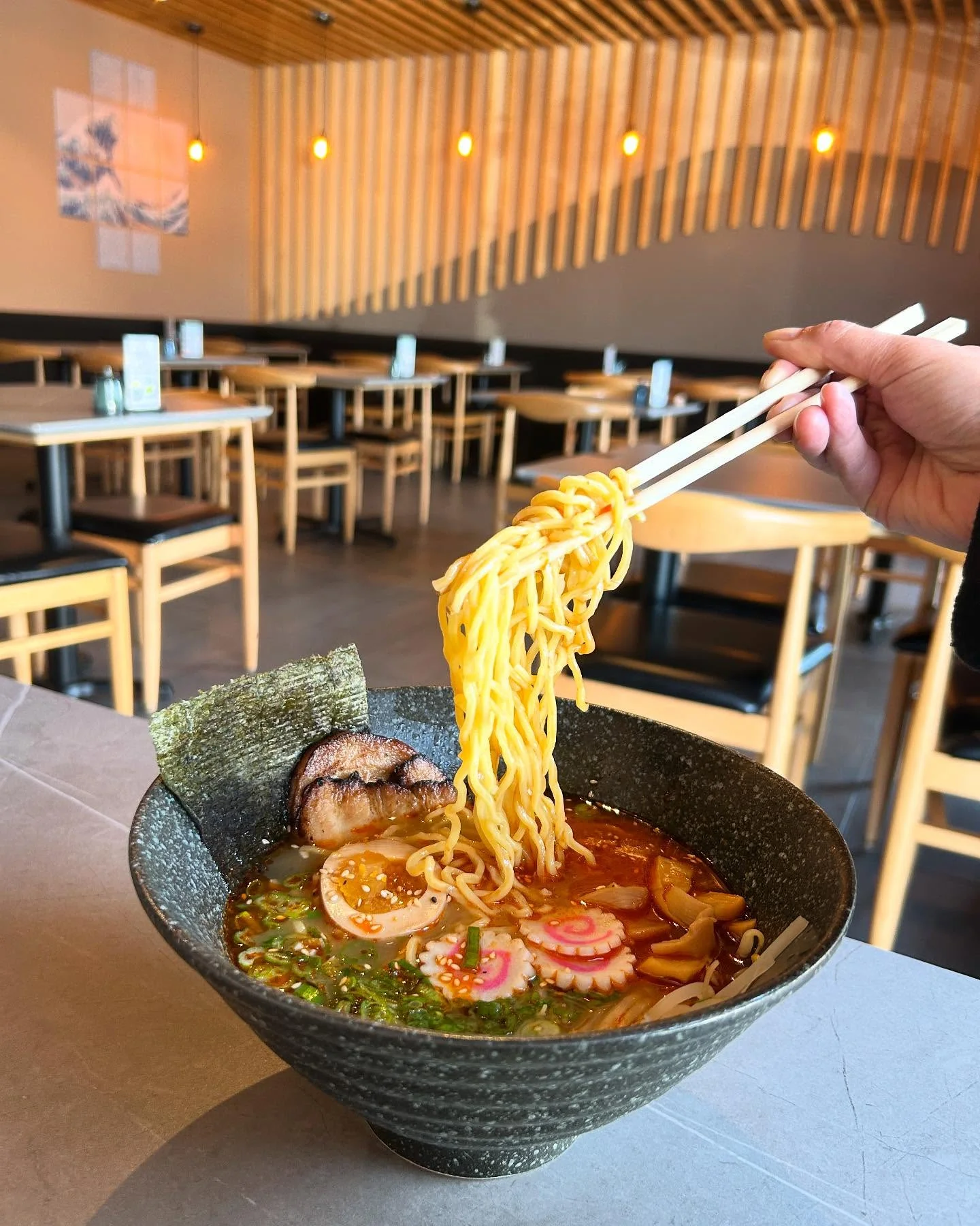 A bowl of ramen with noodles being lifted by chopsticks, surrounded by an inviting dining atmosphere.