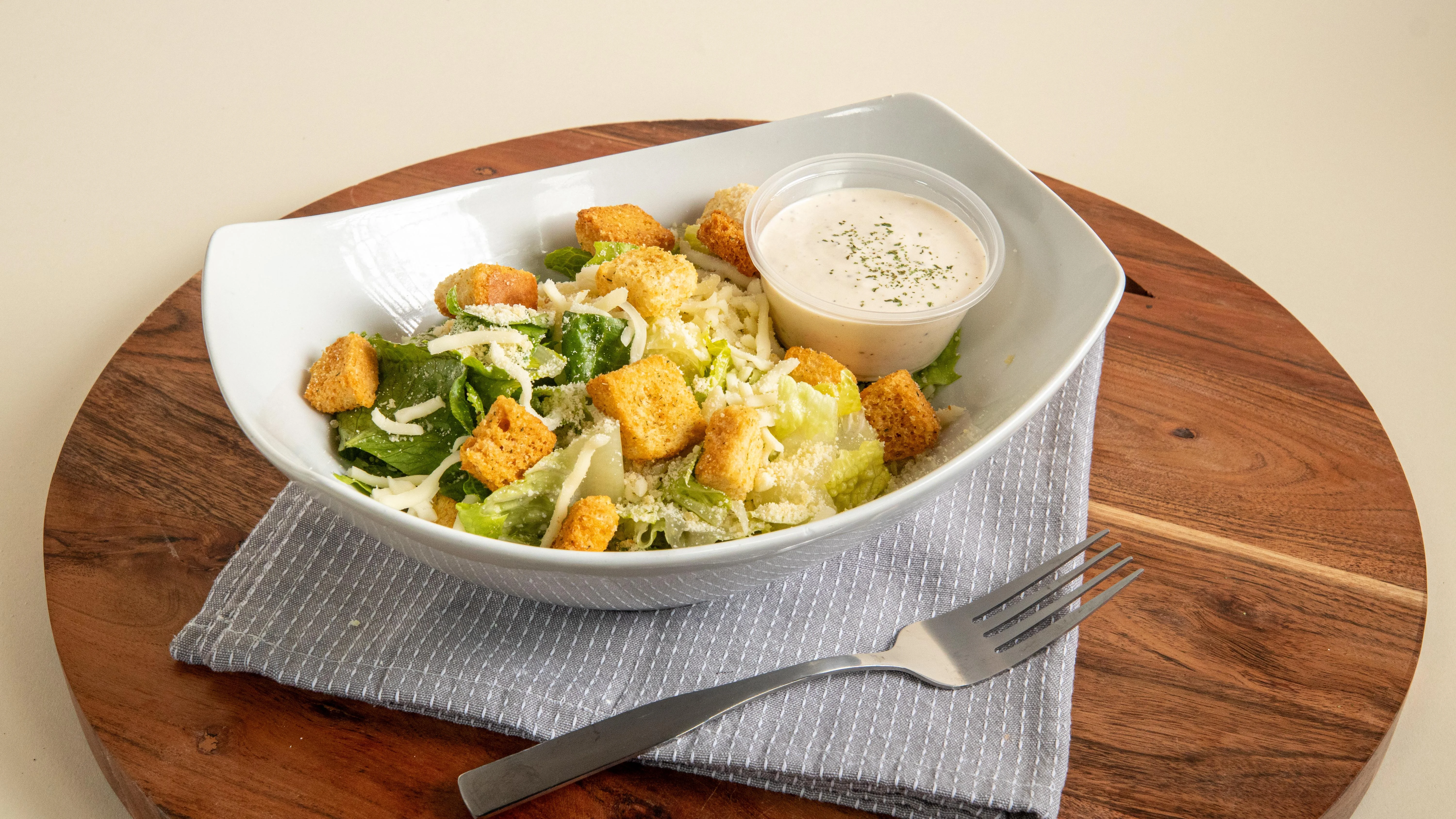 A Caesar salad served in a bowl with lettuce, croutons, and a side of dressing.