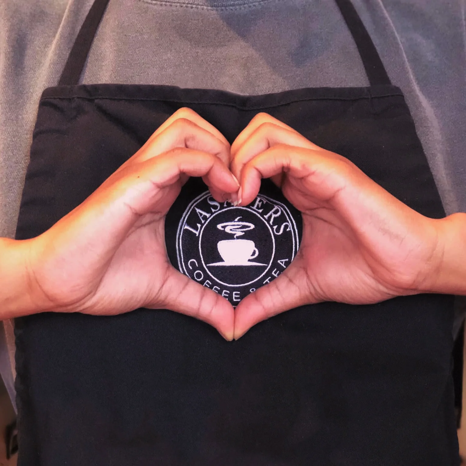 Barista wearing apron with hands in heart shape.