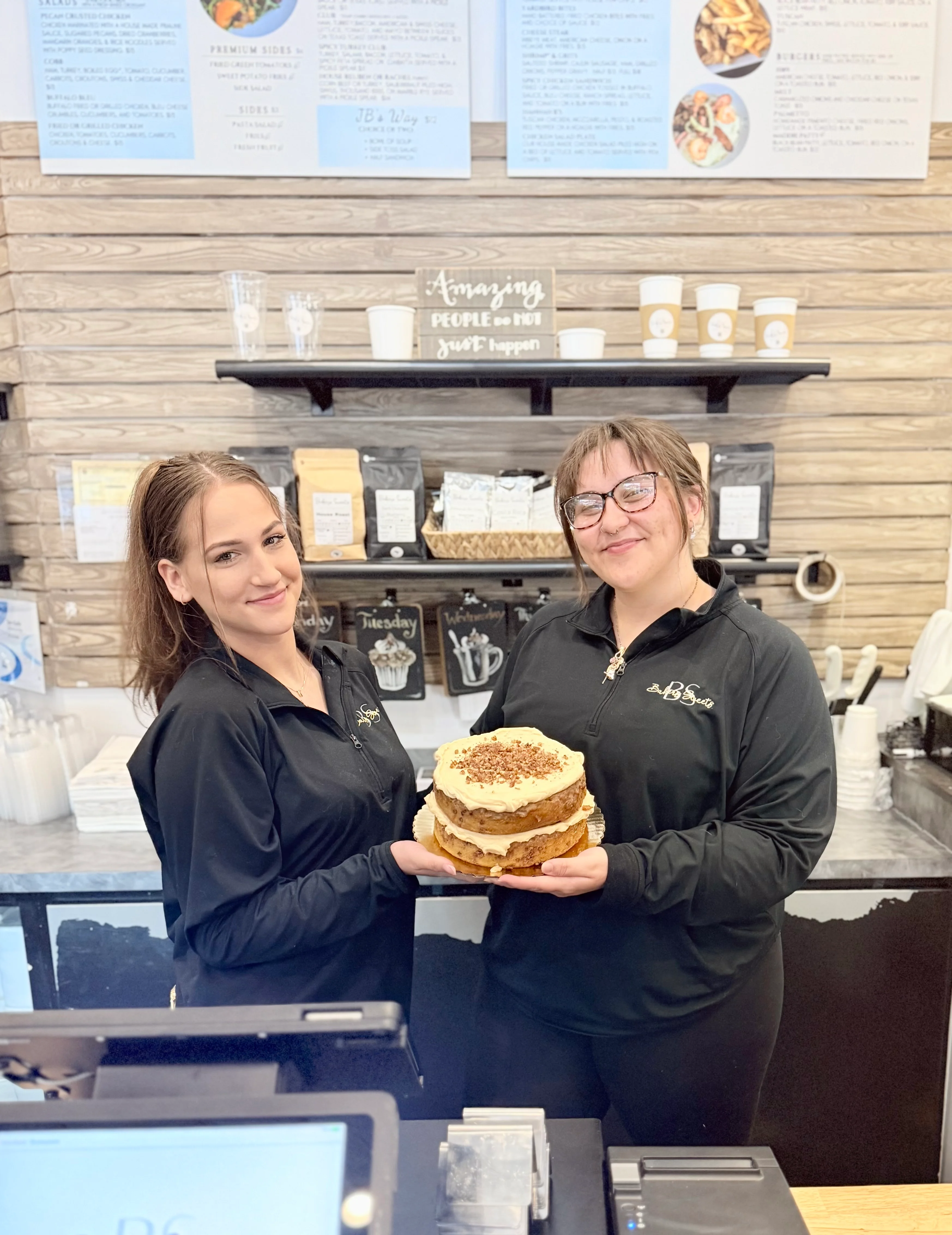 Restaurant staff holding a decorated layered cake inside a bakery cafe