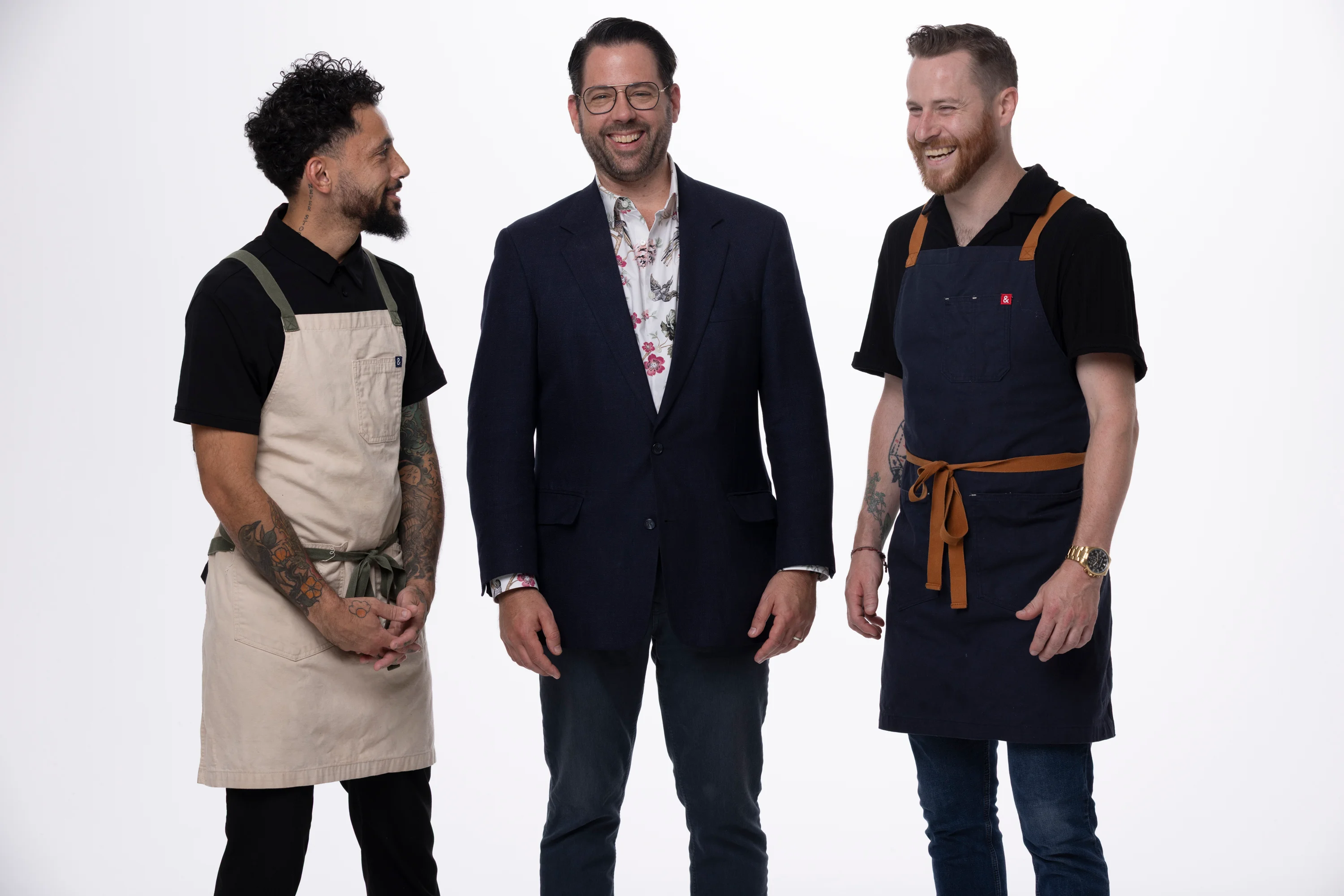 Three chefs in aprons smiling together in a studio setting