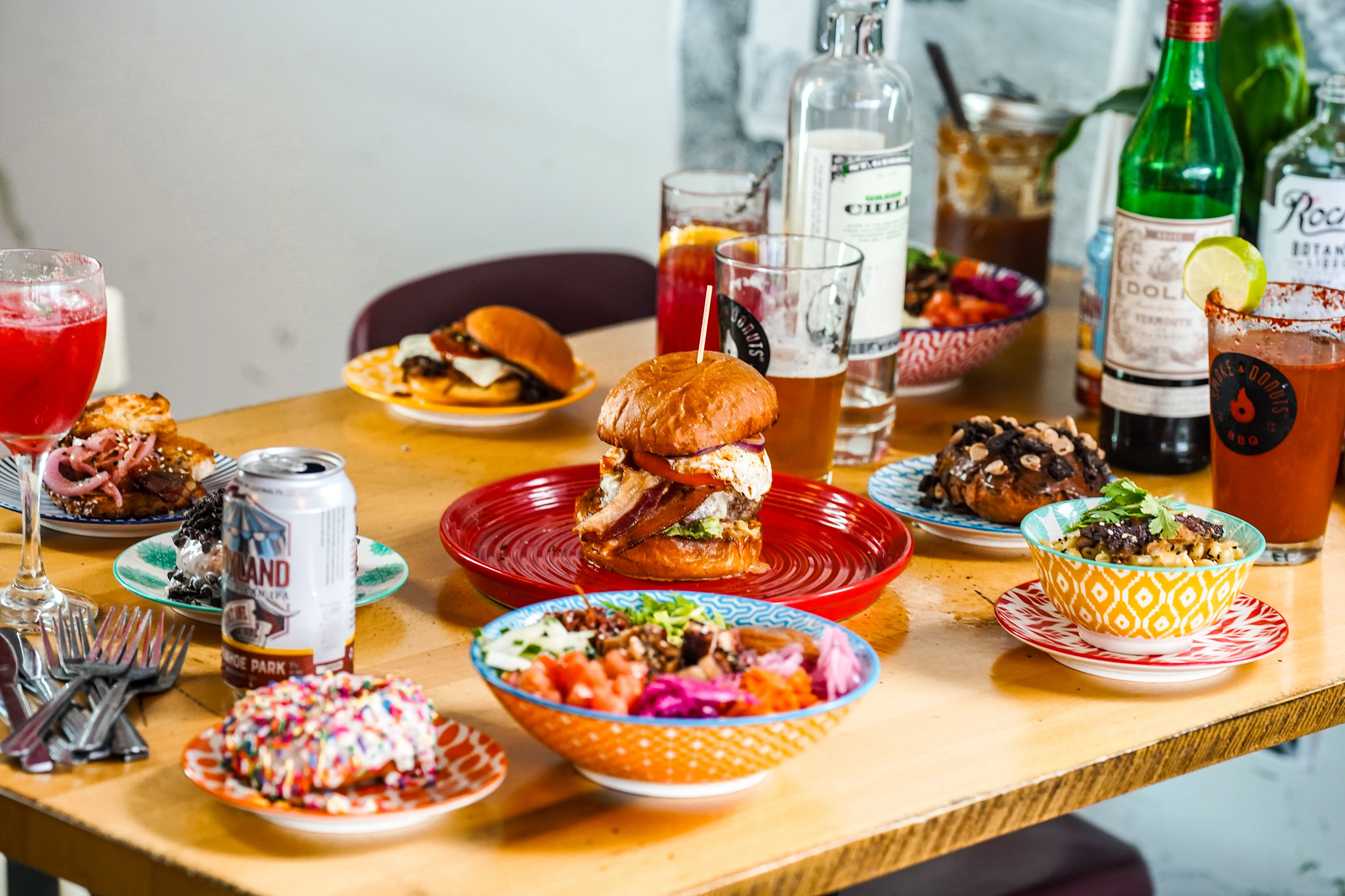 A table with drinks, food, and multi-colored plate in the Smoke & Donuts restaurant space