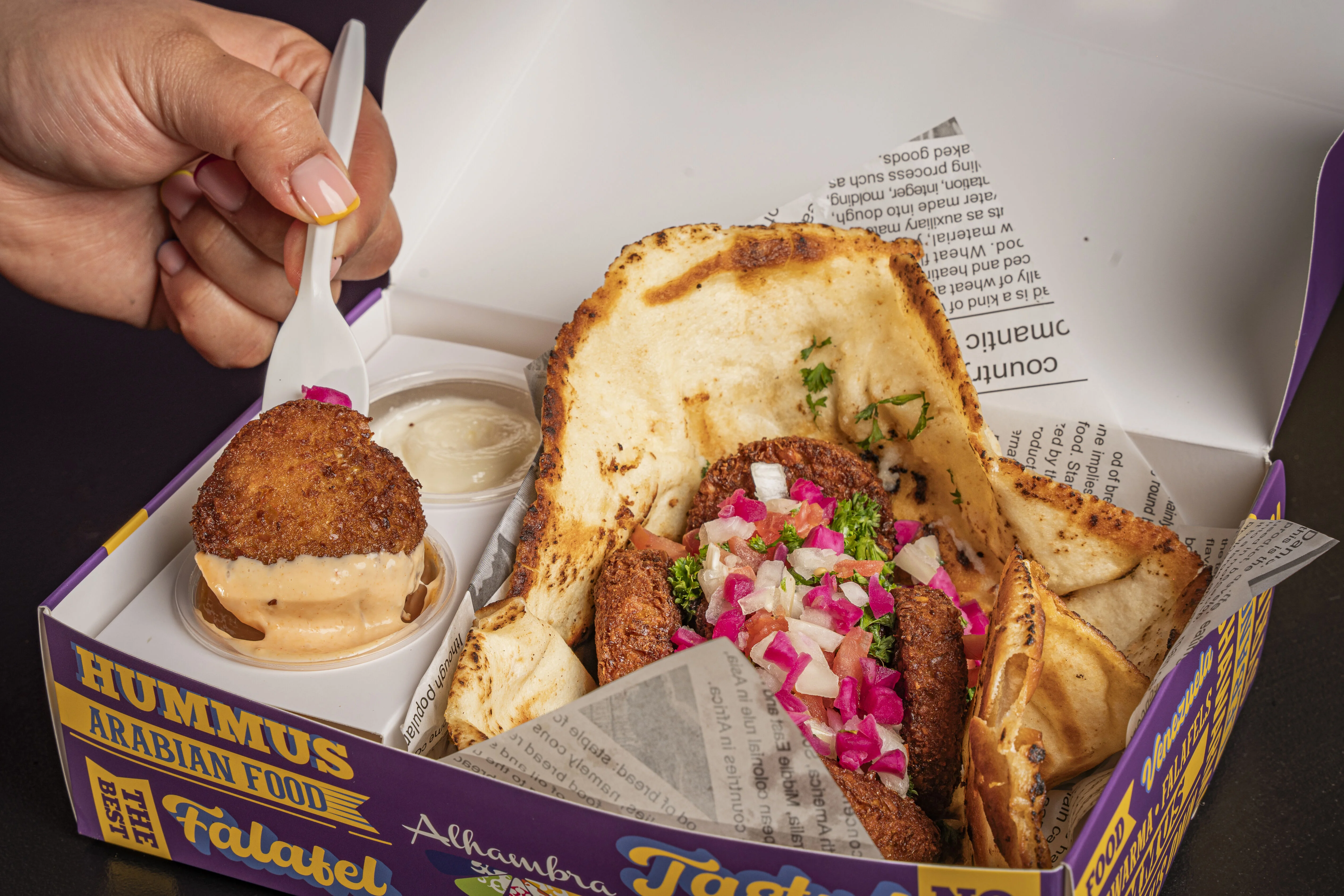 A box of falafel with pita, toppings, and a dipping sauce.