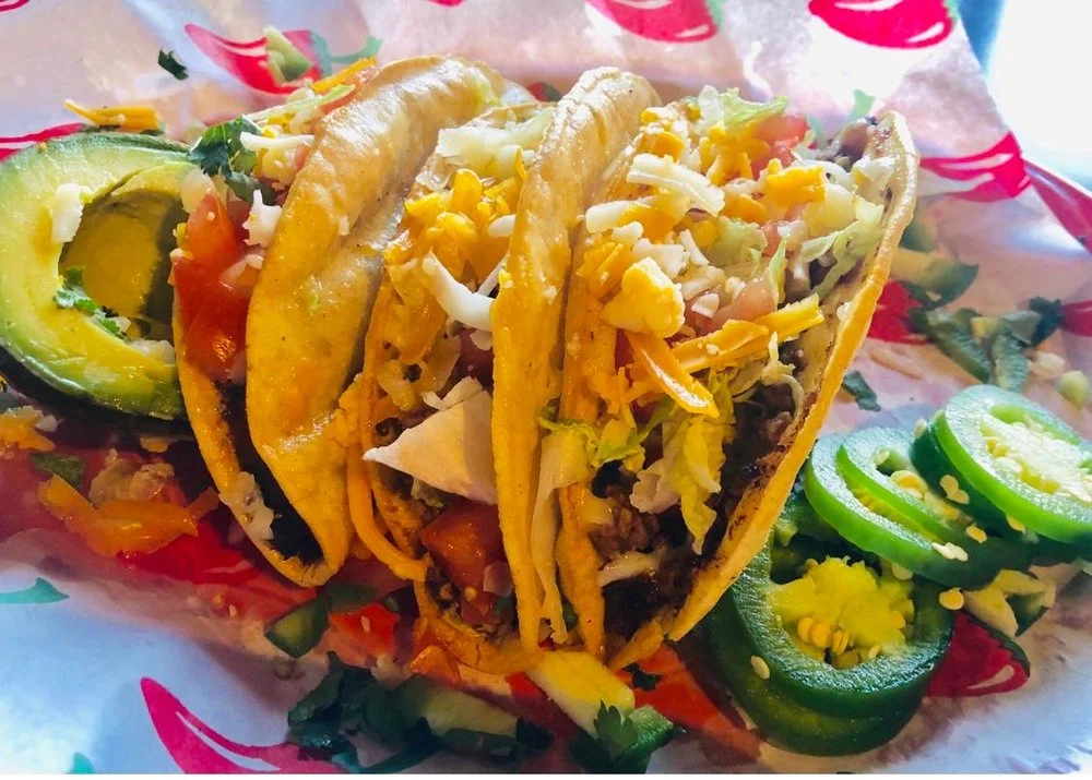 Three delicious Mexican tacos served with avocado and jalapeños