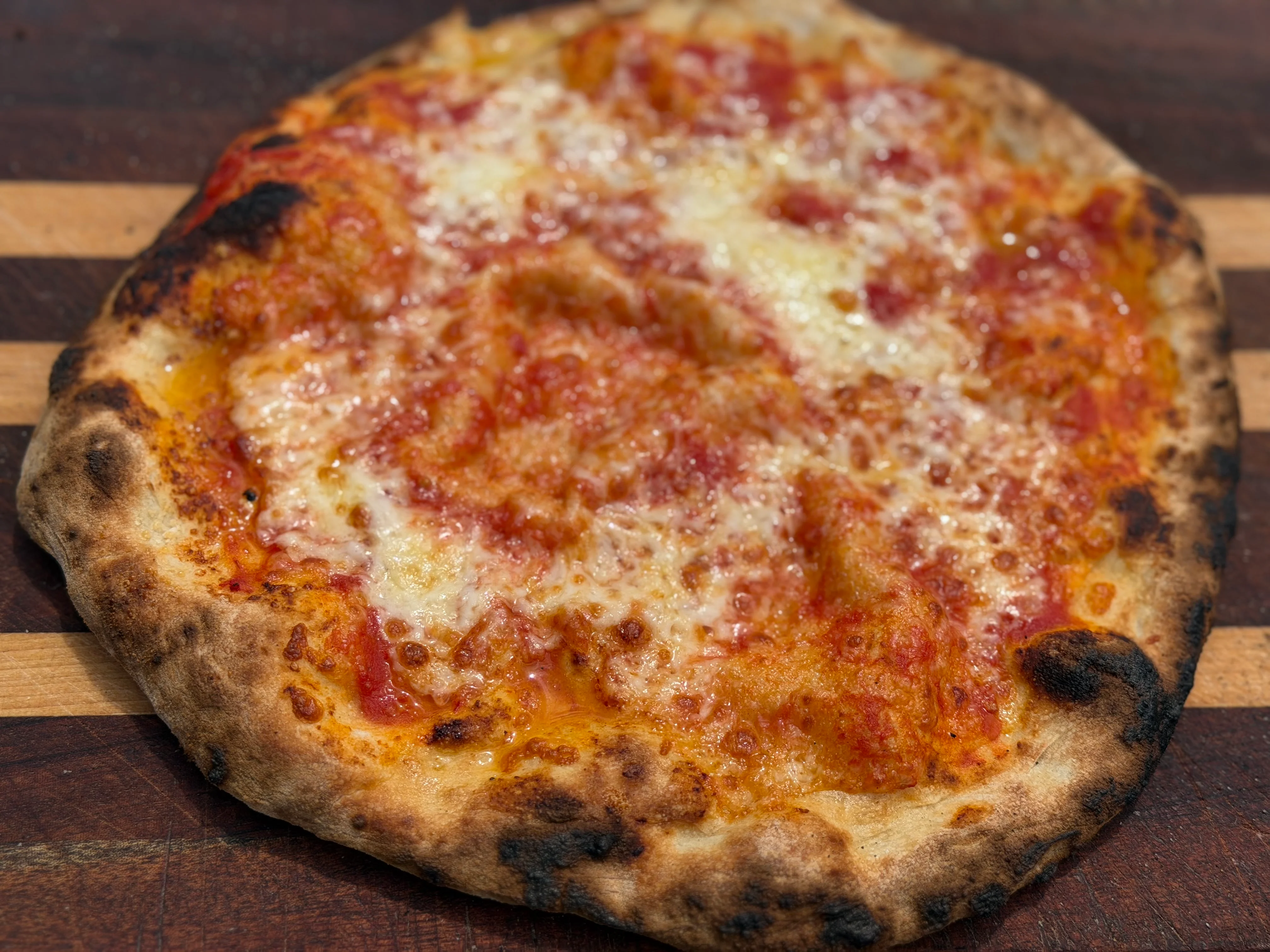 A close-up of a delicious pizza featuring a chewy crust, tomato sauce, and melted cheese, set on a wooden board.