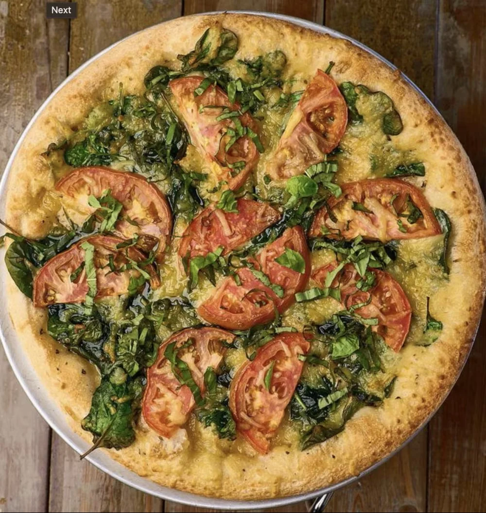 A freshly baked pizza topped with fresh tomatoes, spinach, and herbs, displaying a golden crust.