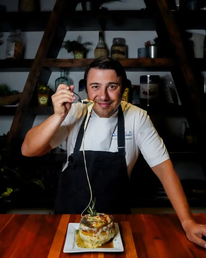 A chef playfully pulls a strand of cheese from a fresh dish, showcasing a beautifully plated culinary creation.