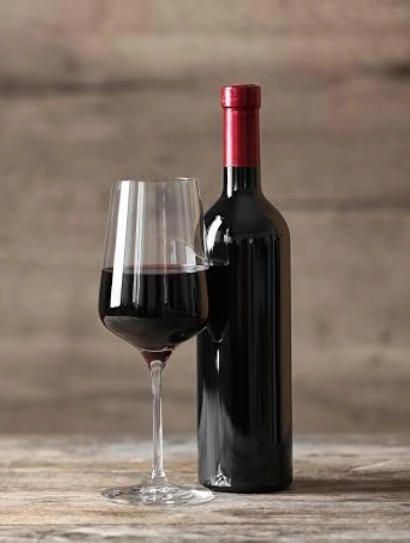 Bottle of red wine with a glass on a rustic wooden table