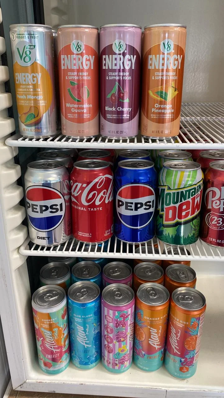 A refrigerated display showcasing various energy drinks, sodas, and flavored beverages. The cans are organized by brand and type.