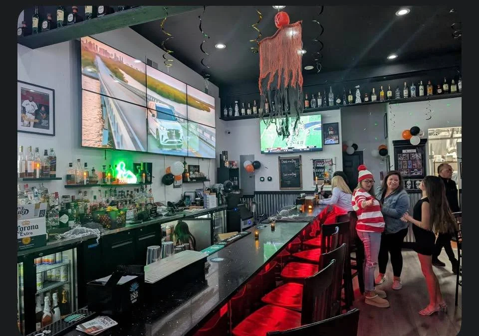 An engaging bar atmosphere decorated with festive elements, featuring multiple screens, a colorful bar, and patrons interacting, creating a social vibe.