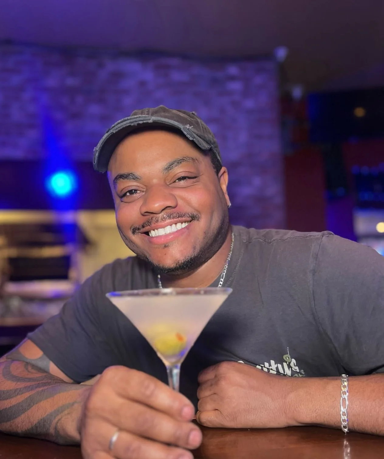 Bartender smiling with a martini cocktail at a vibrant bar