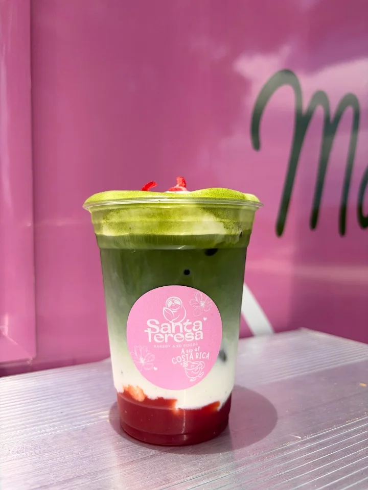A colorful layered beverage showcasing green matcha, creamy milk, and a red fruit base, topped with decorative bits.